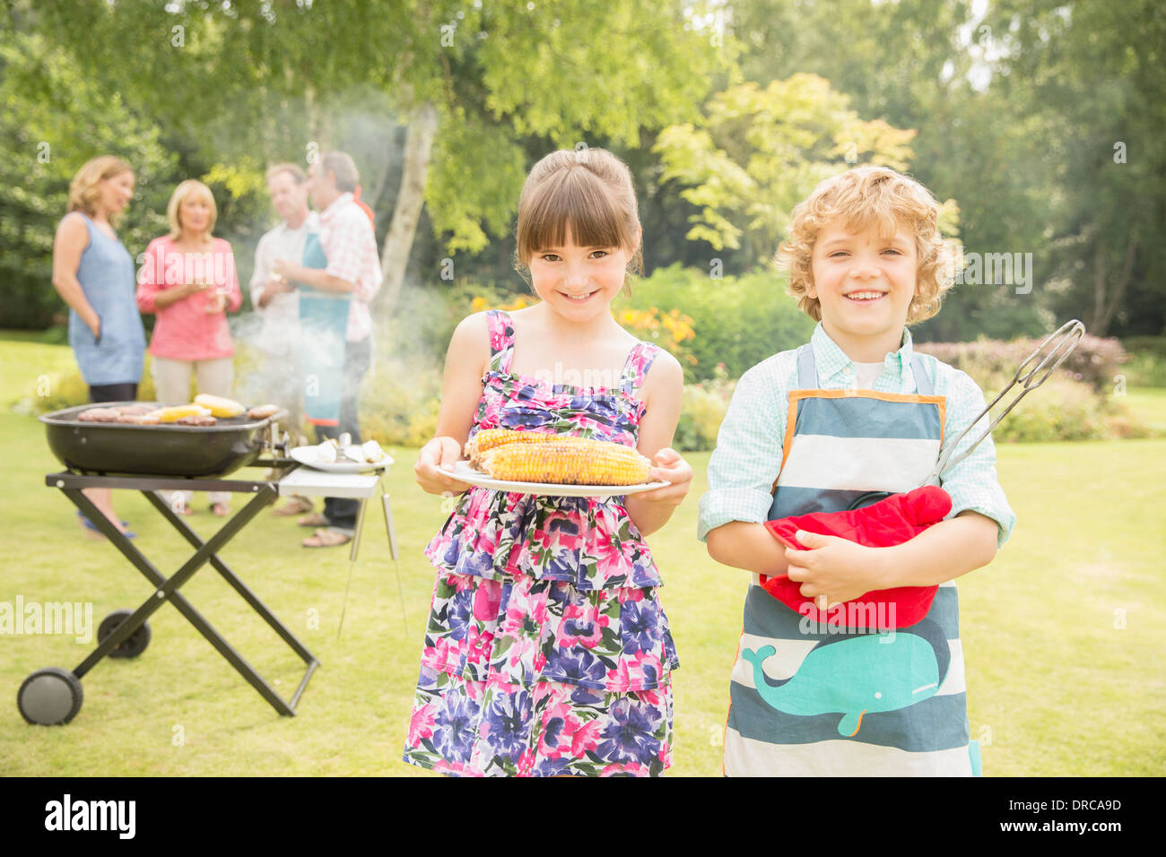 Bruder und Schwester mit gegrilltem Mais in der Nähe von Grill im Garten Stockfoto