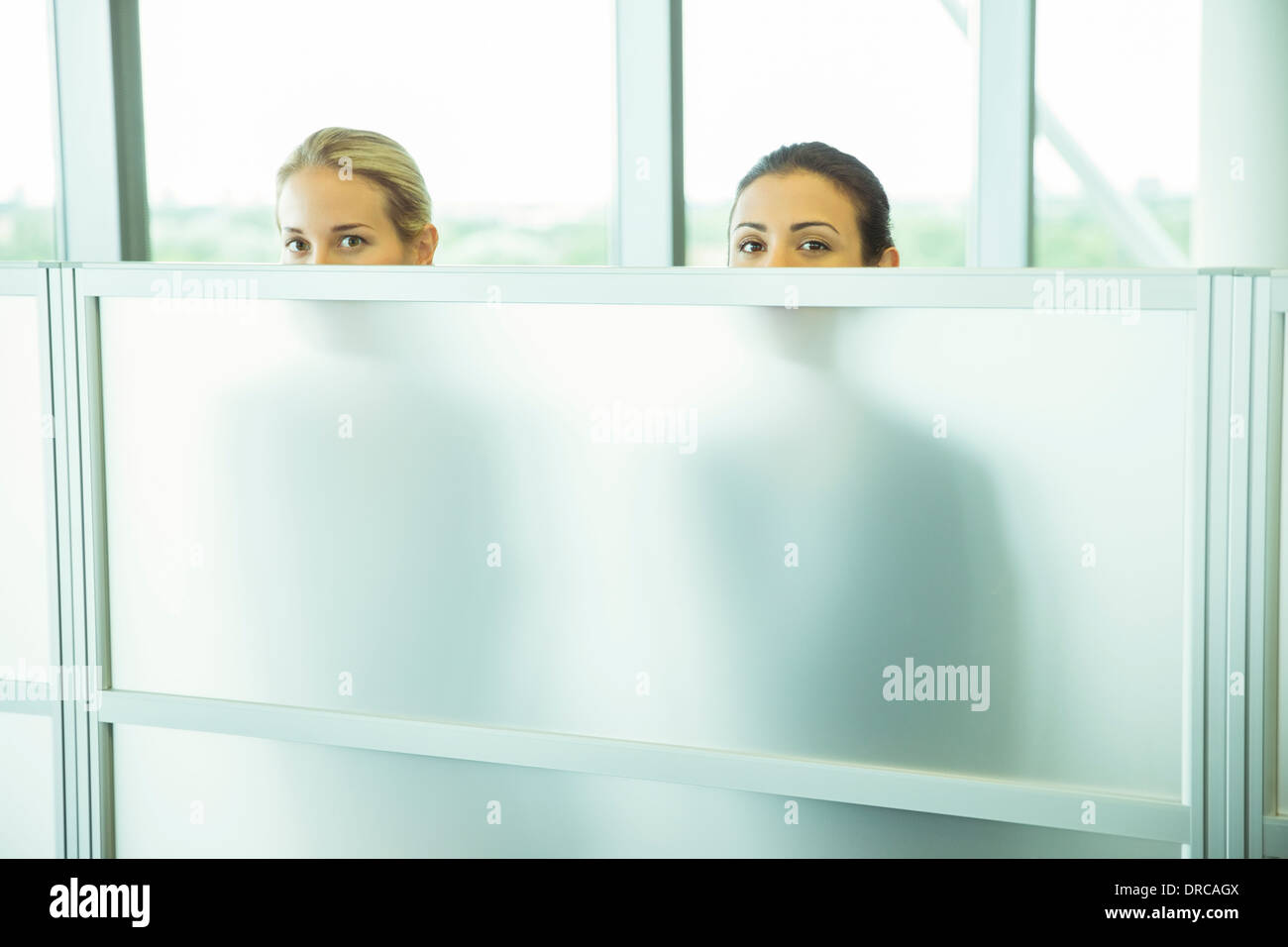 Geschäftsfrauen spähen über eine halbe Wand im Büro Stockfoto