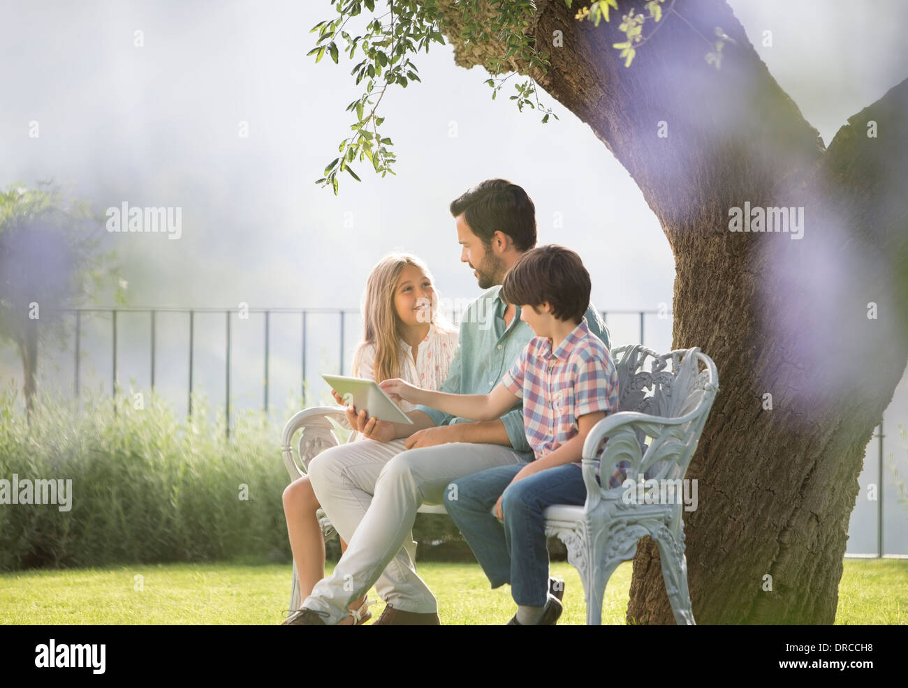 Vater und Kinder mit digital-Tablette auf Bank im park Stockfoto
