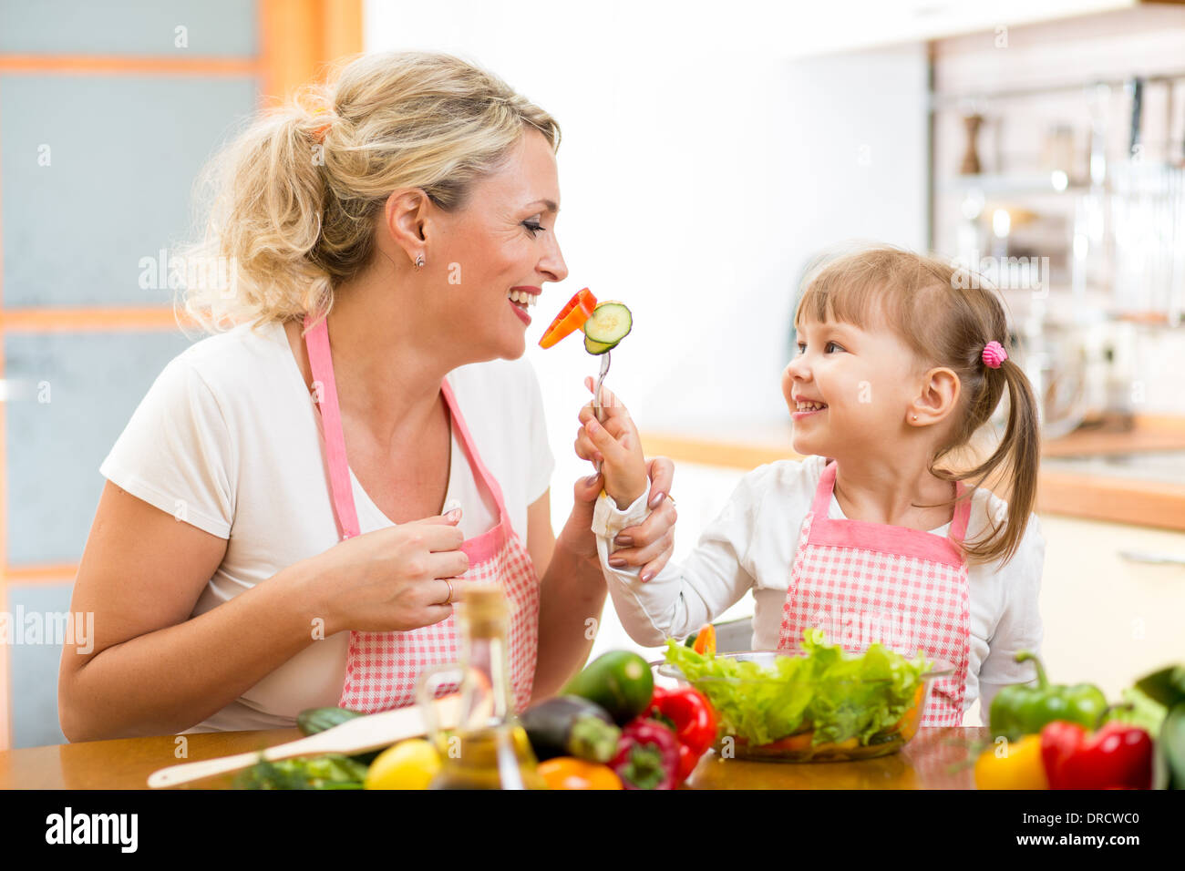 junge Tochter Fütterung Mutter Gemüse in der Küche Stockfoto