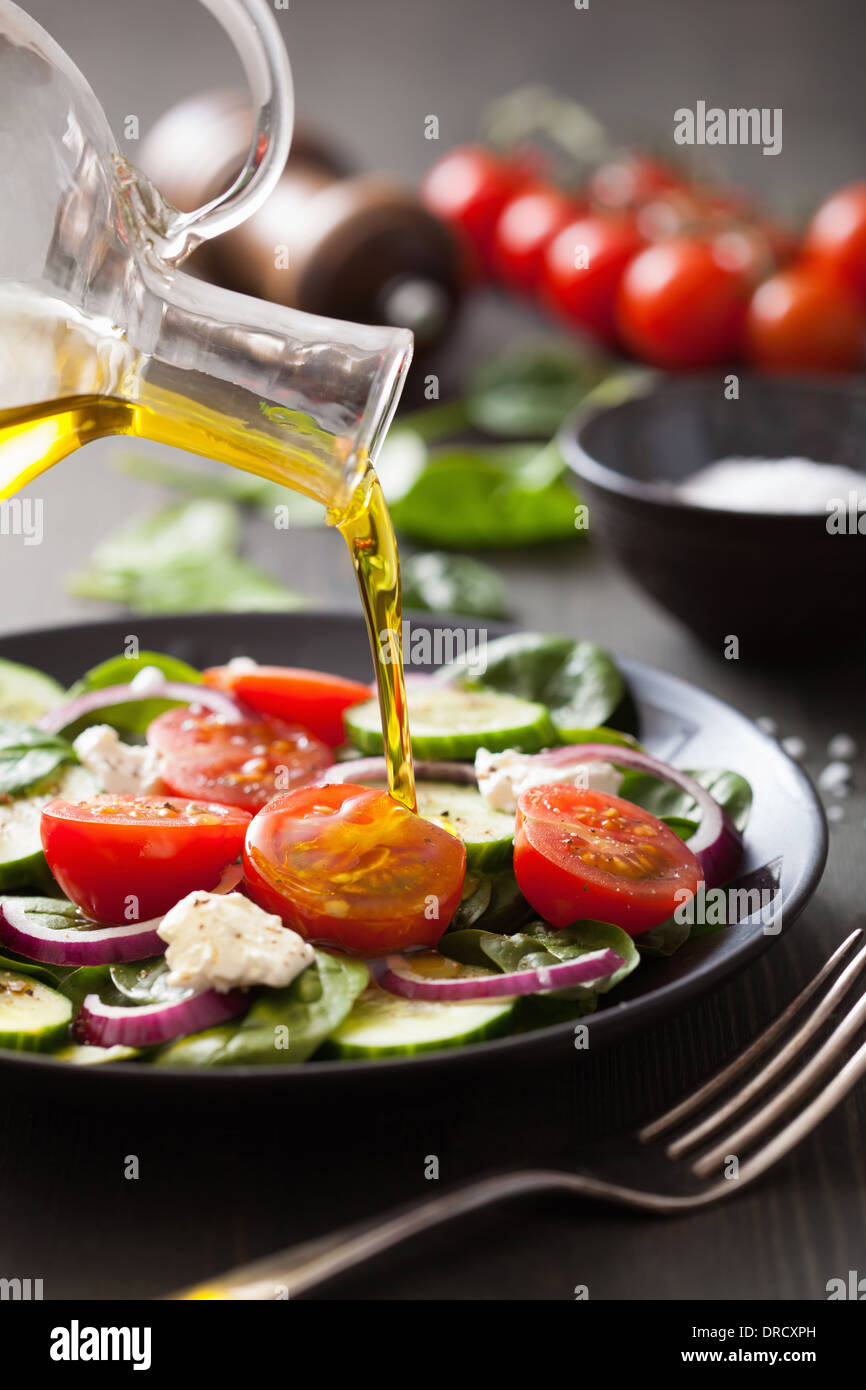 Gießen Olivenöl auf Salat mit Tomaten und Gurken Stockfoto