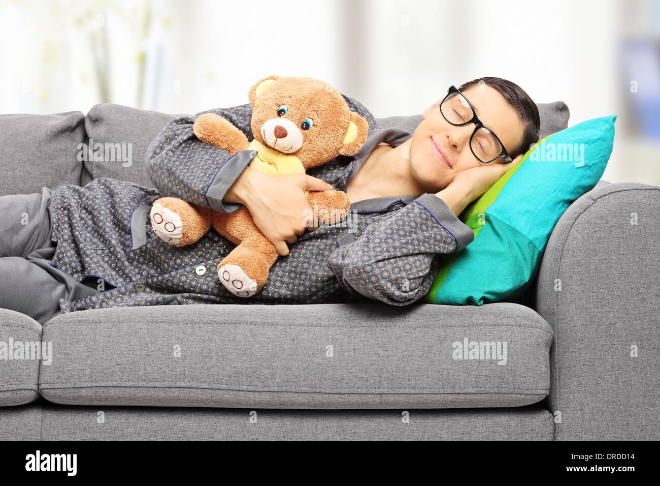 Junger Mann hält Teddybär und ein Nickerchen auf der Couch zu Hause Stockfoto