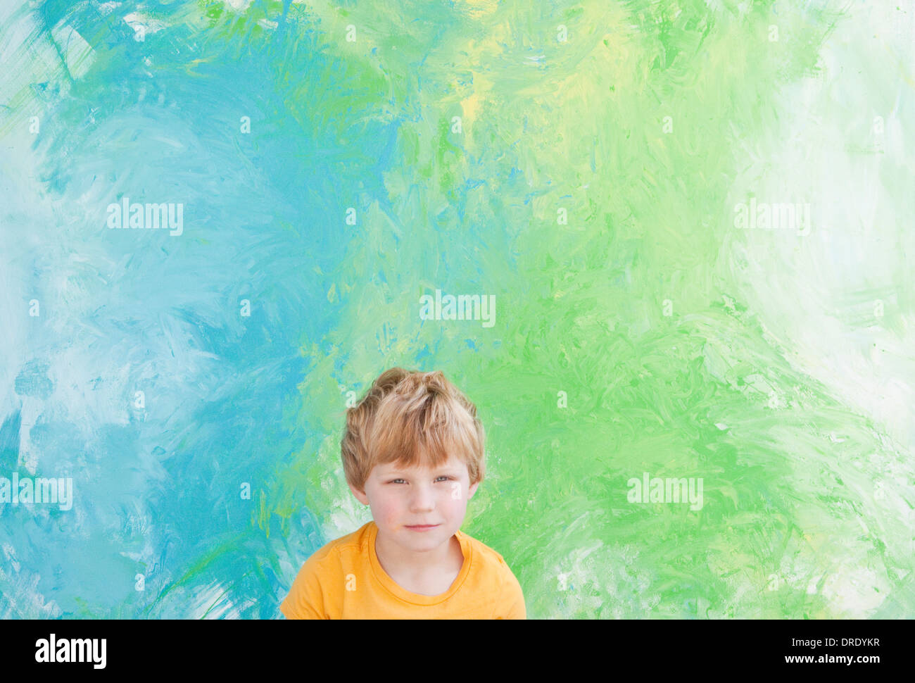 Kleiner Junge sitzt vor Grün und blau Malerei Stockfoto
