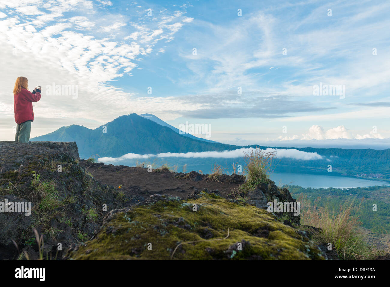 Junge Frau nehmen Momentaufnahme des Lake Batur und Mount Agung mit ihrem Smartphone in Bali bei Sonnenaufgang Stockfoto