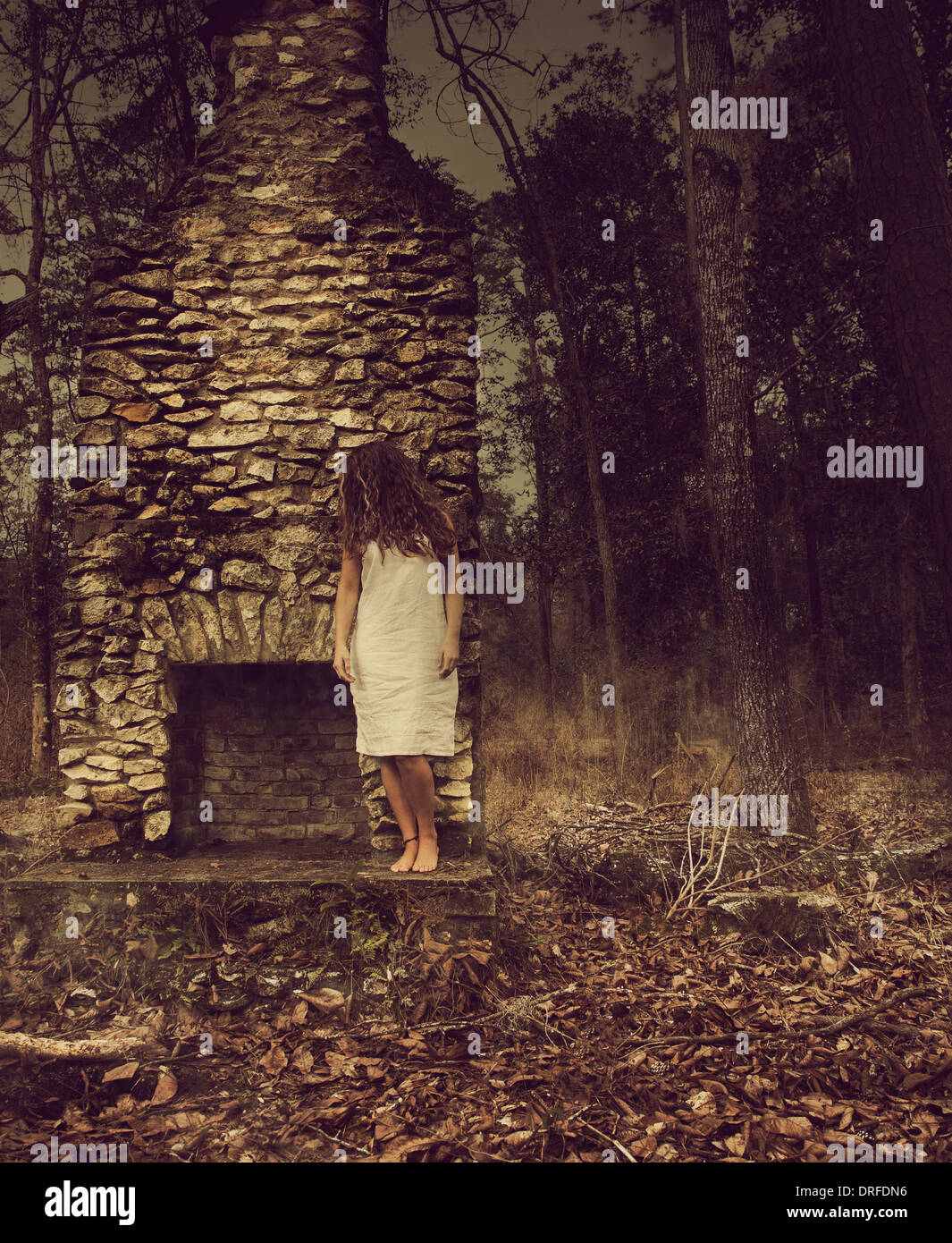 Frau lehnt sich an Steinkamin im Wald Stockfoto