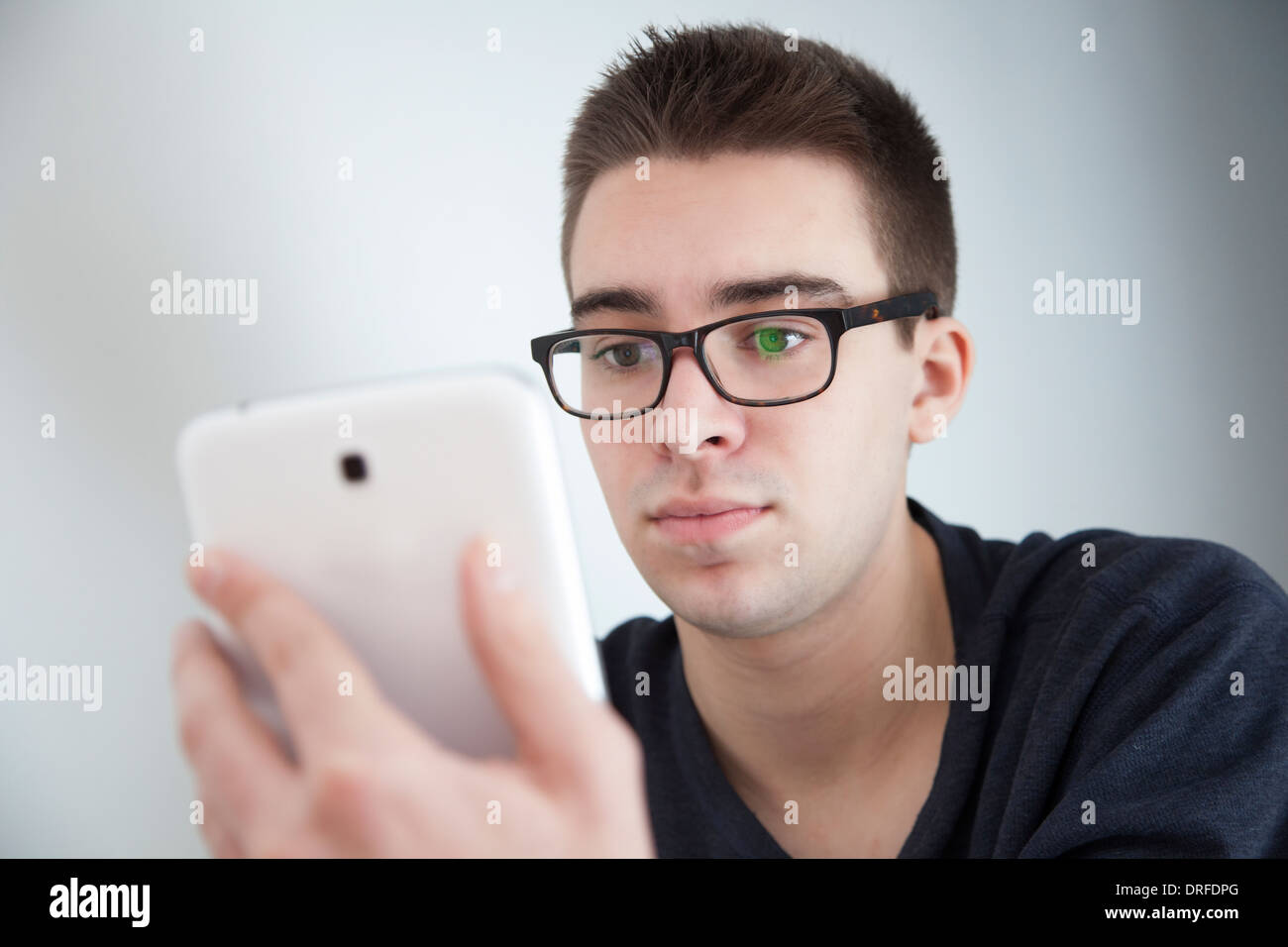 Gut aussehender junger Mann mit Brille, leichte Reflexion. Halten eine weiße digitale-Tablette. Ernsten Ausdruck. Stockfoto
