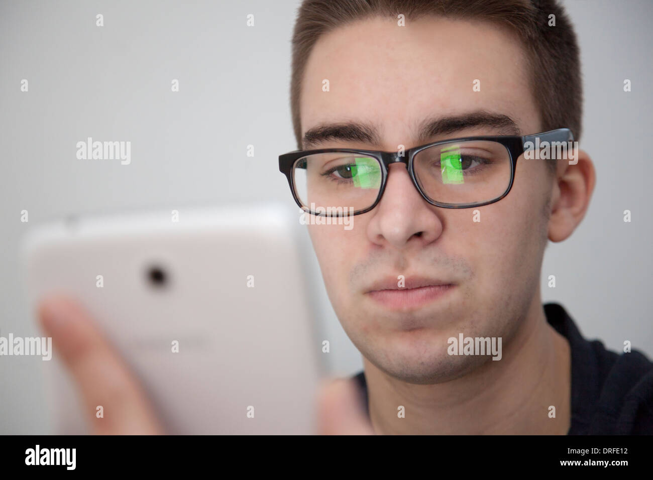 Gut aussehender junger Mann mit Brille, leichte Reflexion. Halten eine weiße digitale-Tablette. Ernsten Ausdruck. Stockfoto