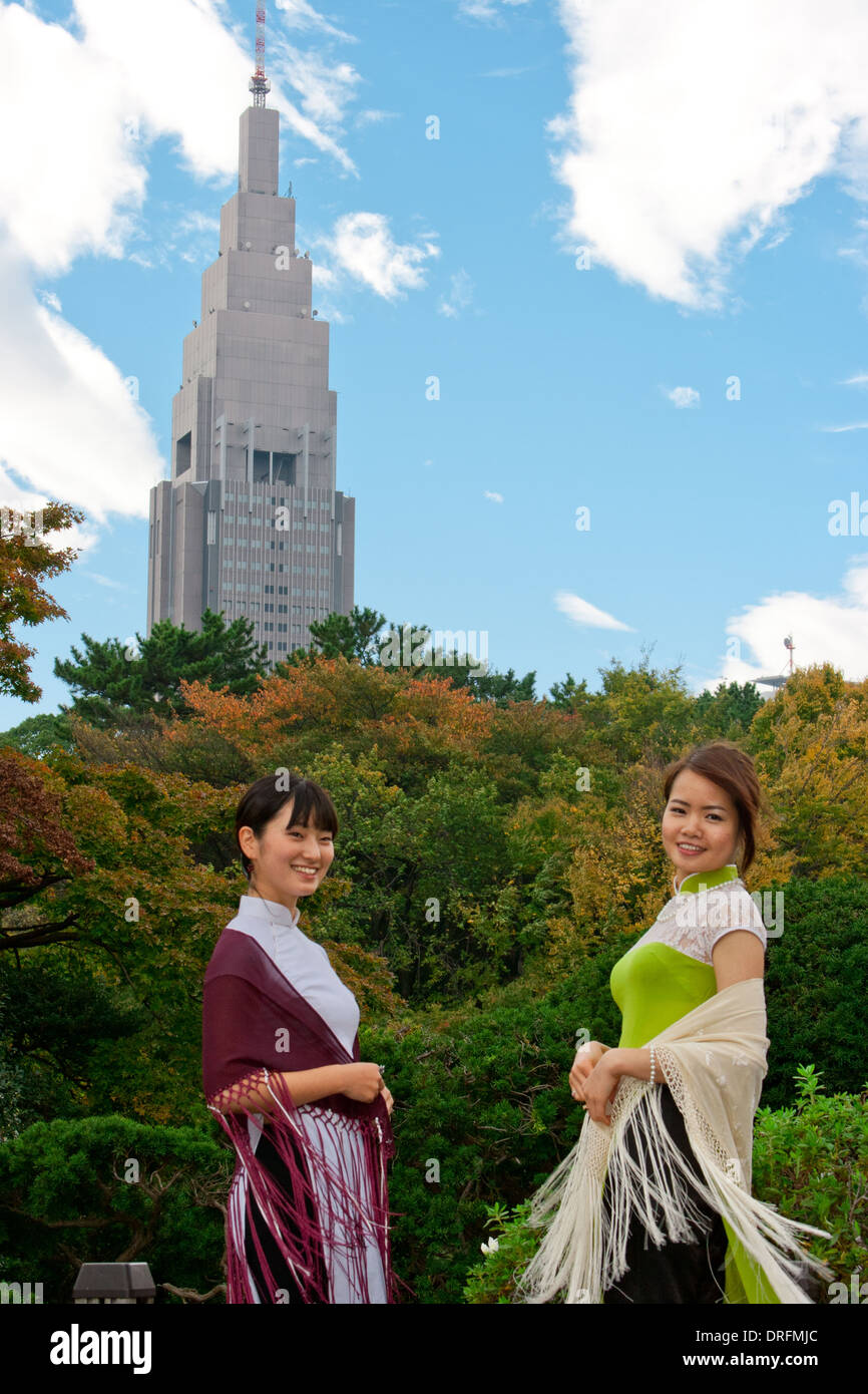 Zwei junge Frauen, die in den traditionellen Ao Dai in Shinjuku Park vor NTT Docomo Yoyogi Gebäude Stockfoto