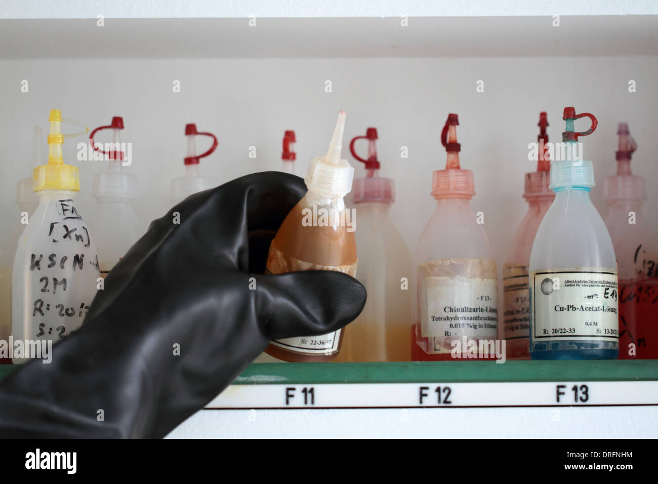 eine Hand mit einem chemischen Handschuh mit einer Sprühflasche auf einem Regal Stockfoto