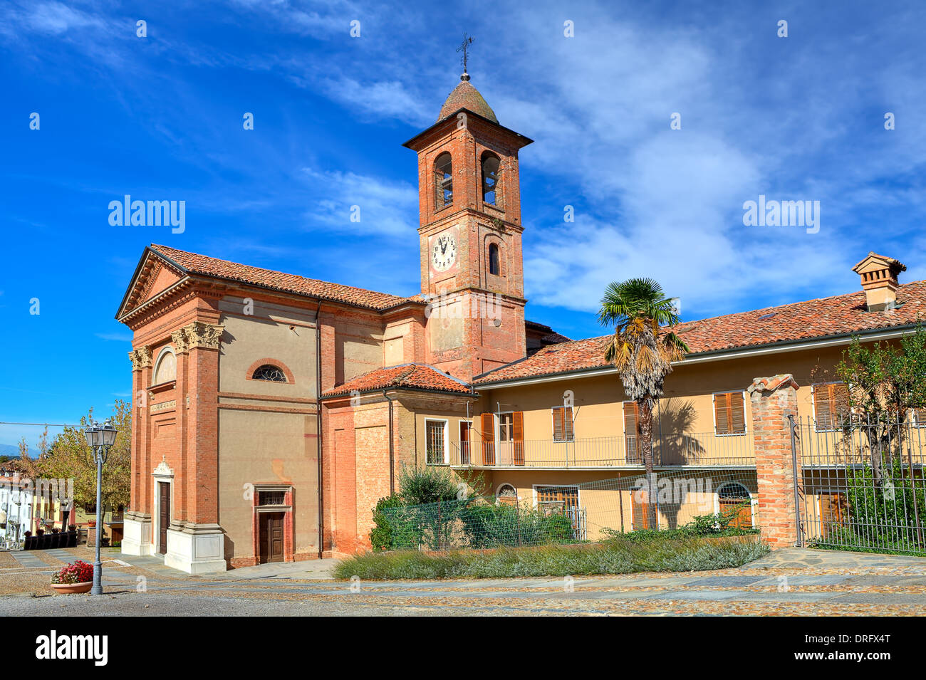 Alte katholische Kirche aus rotem Backstein am Stadtplatz unter blauem Himmel im kleinen Ort Grinzane Cavour in Piemont, Italien. Stockfoto
