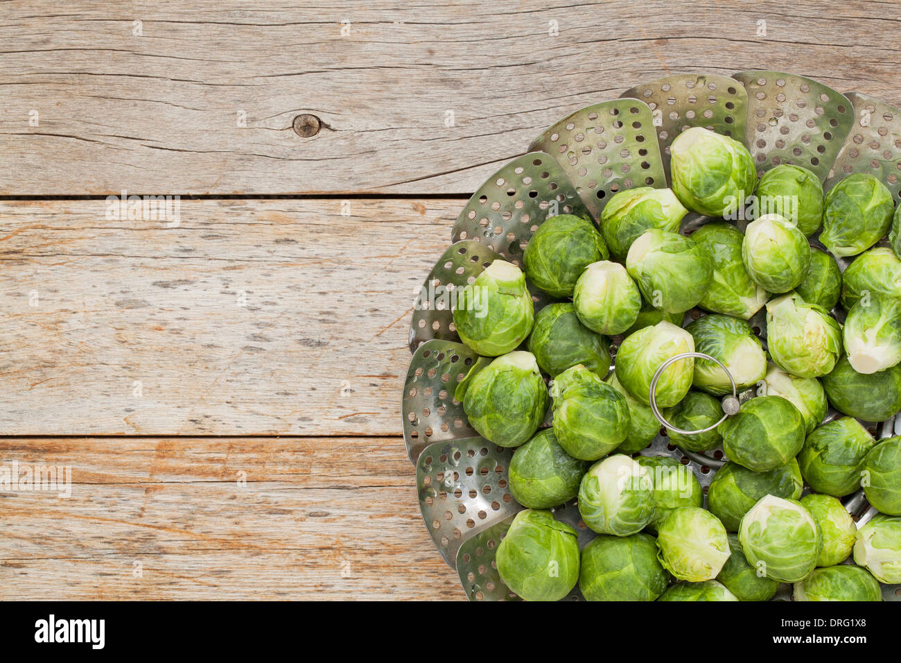 frischer Rosenkohl in einem Metall Dämpfeinsatz auf rustikalen Holztisch Stockfoto