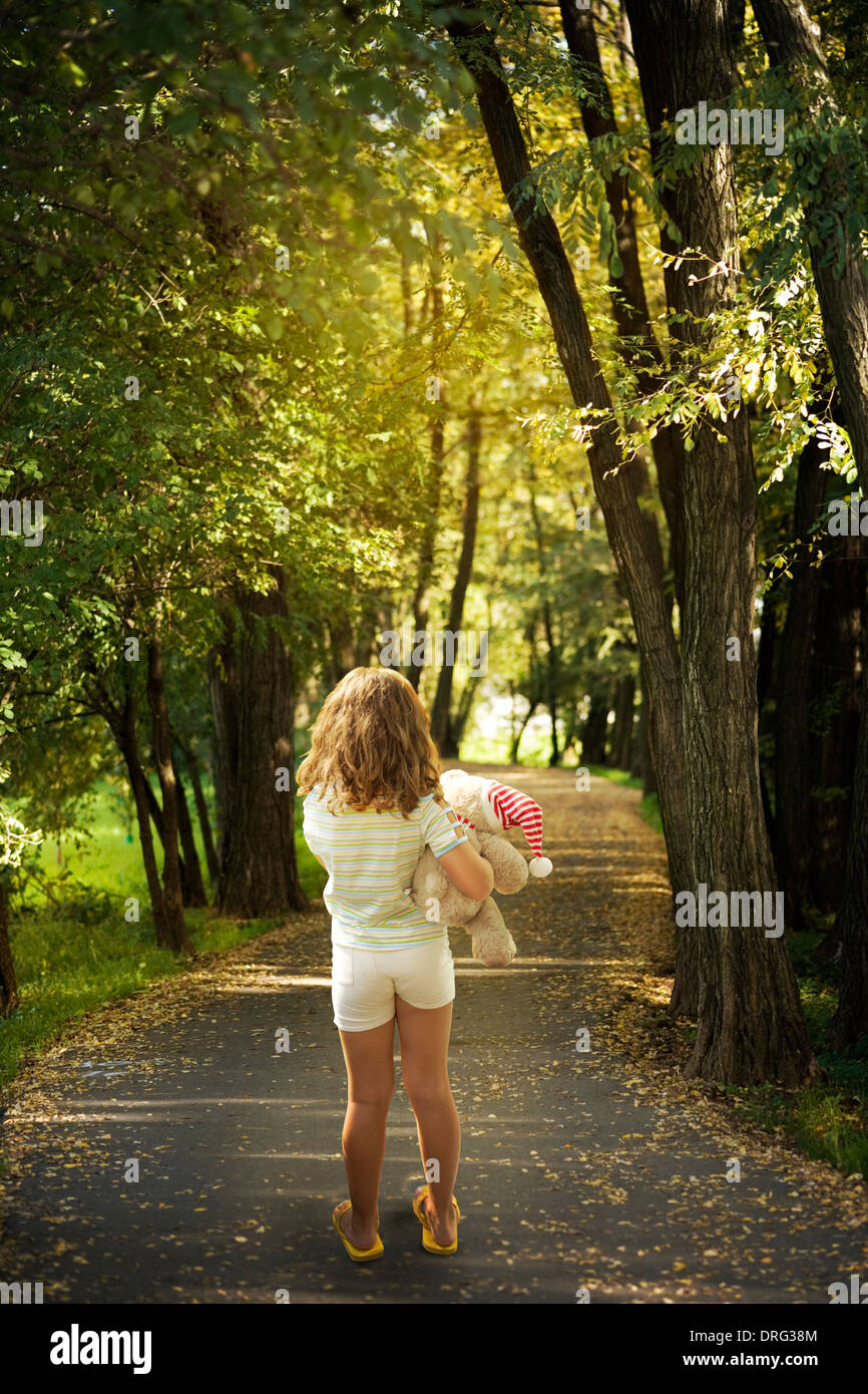 Kleines Mädchen mit Teddy Bär zu Fuß unter den Bäumen Stockfoto