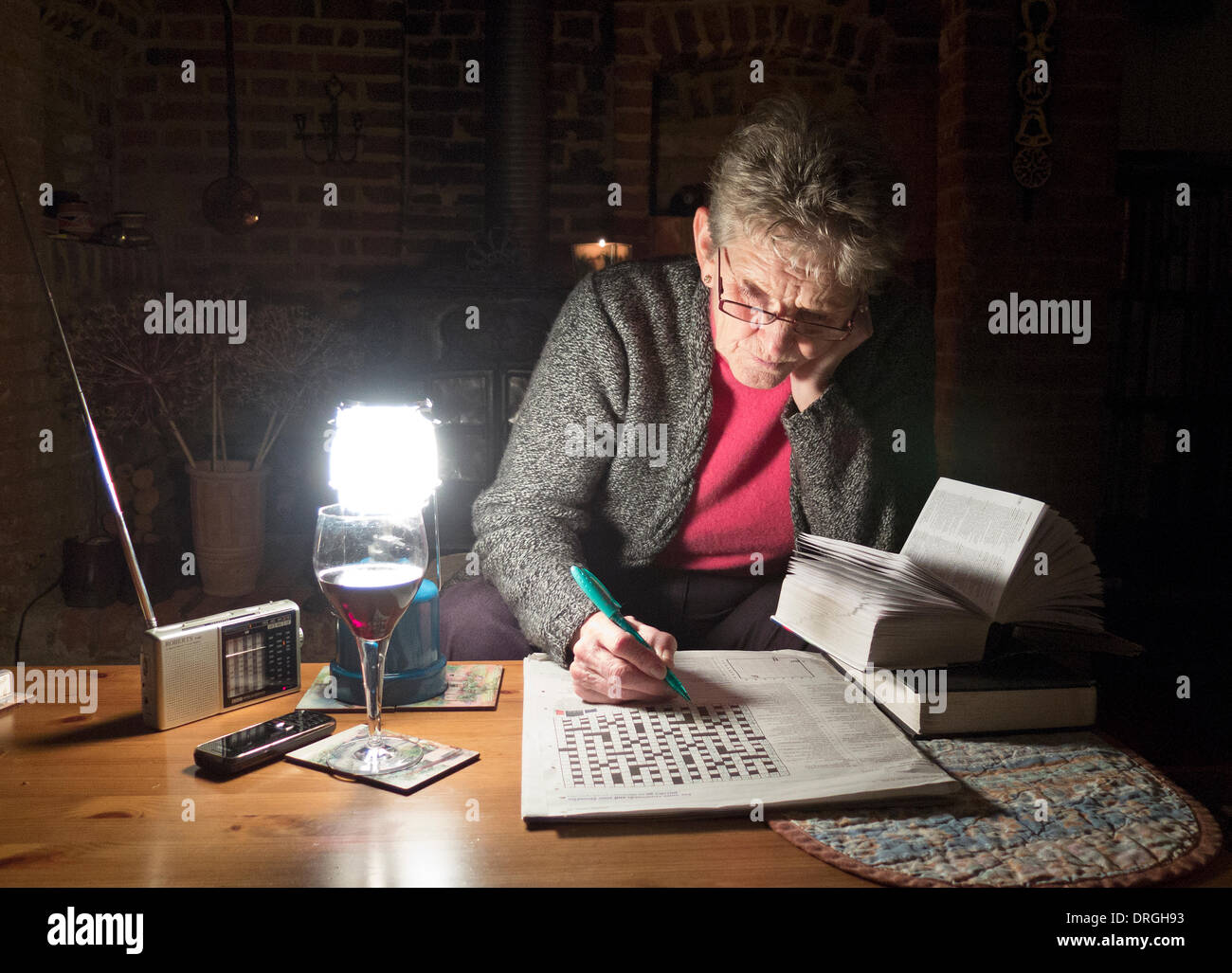 Stromausfälle in Hampshire UK Seniorin Zeitvertreib mit einem Glas Wein, eine tragbare Gas-Licht und Kreuzworträtsel. Stockfoto