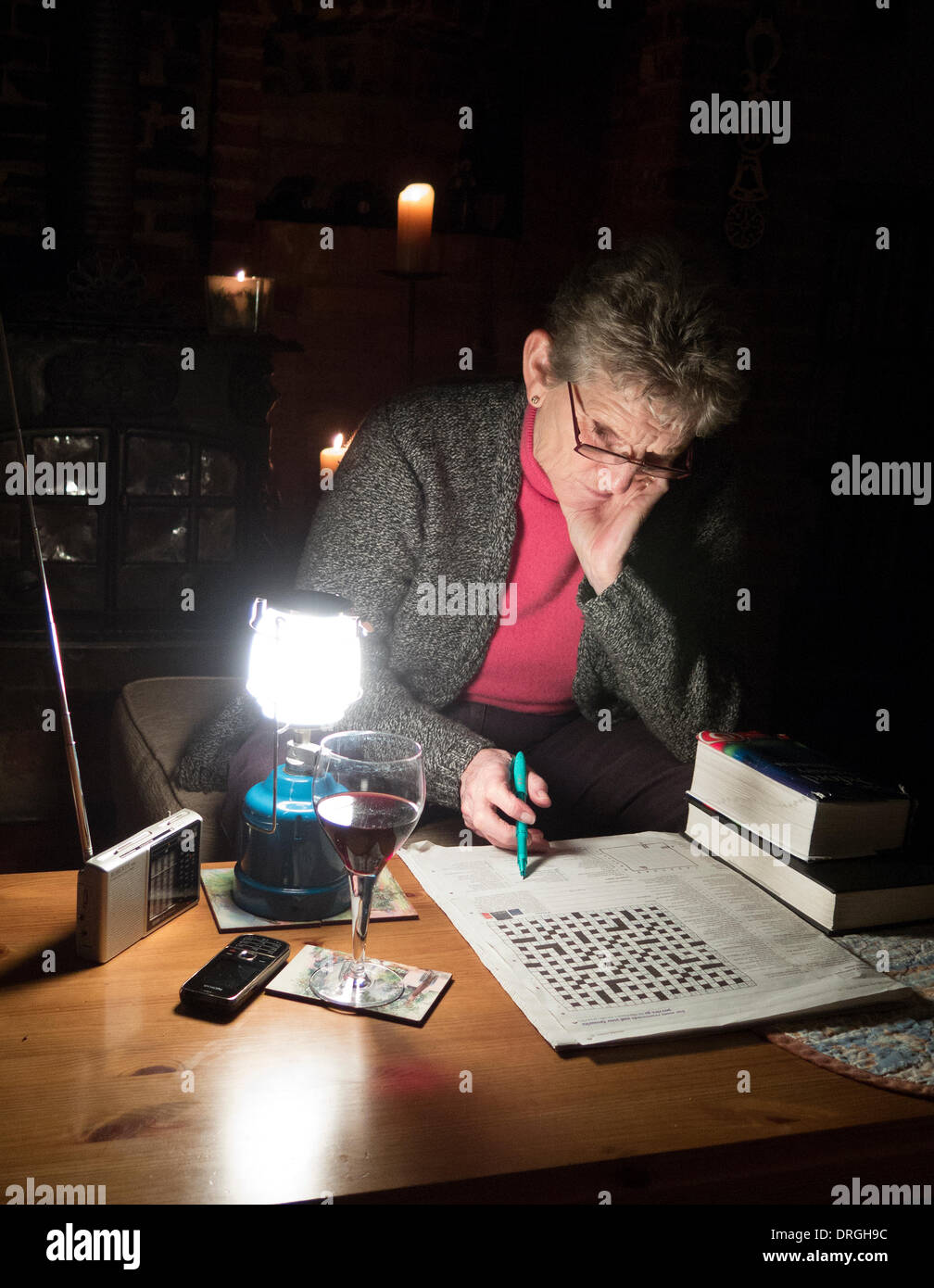 Stromausfälle in Hampshire UK Seniorin Zeitvertreib mit einem Glas Wein, eine tragbare Gas-Licht und Kreuzworträtsel. Stockfoto