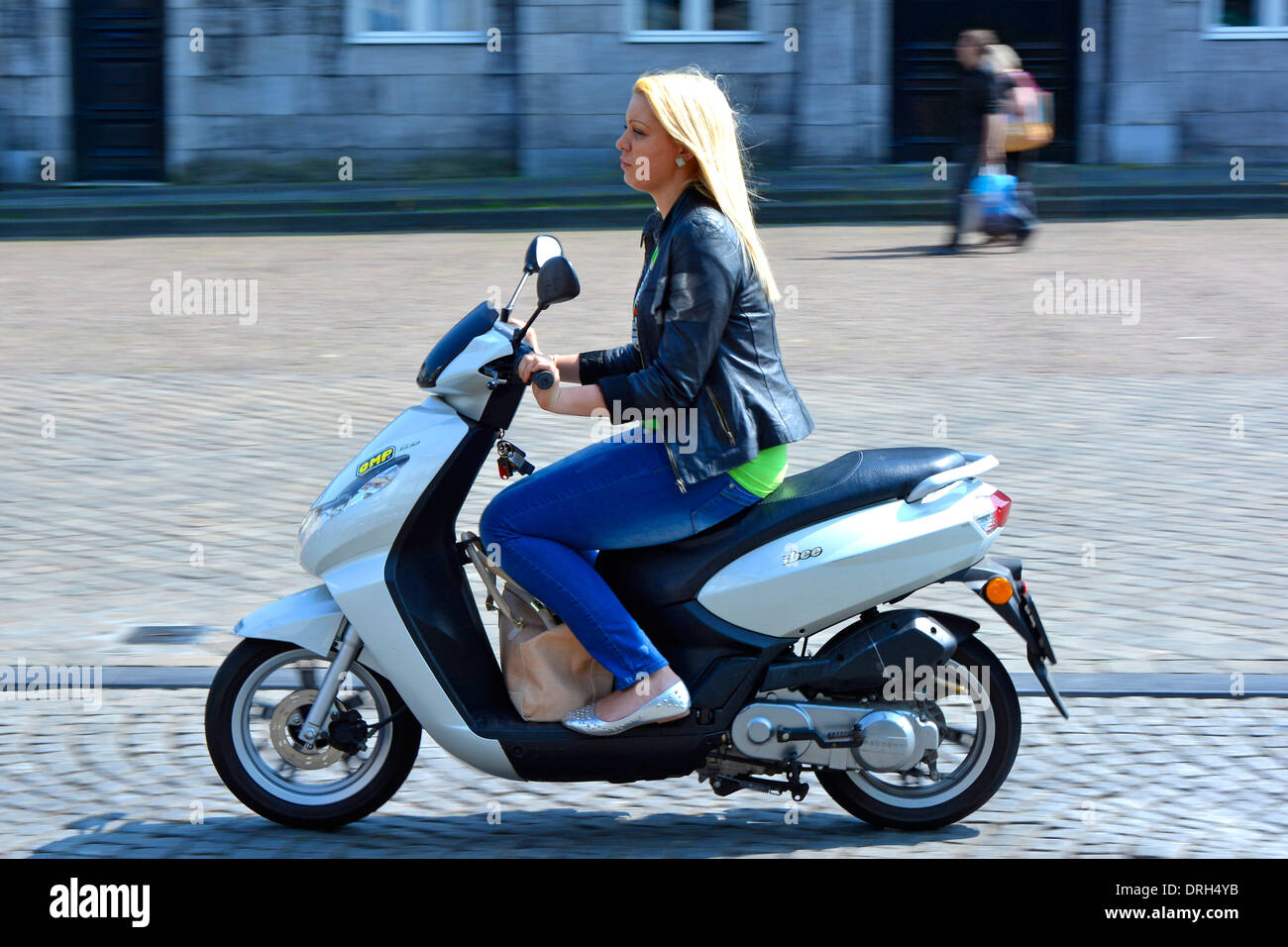 Maastricht City Seitenansicht junge Frau lange blonde Haare reitend Motorroller Handtasche zwischen ihren Füßen warm Juli sonniger Tag Limburg, Niederlande Europa EU Stockfoto