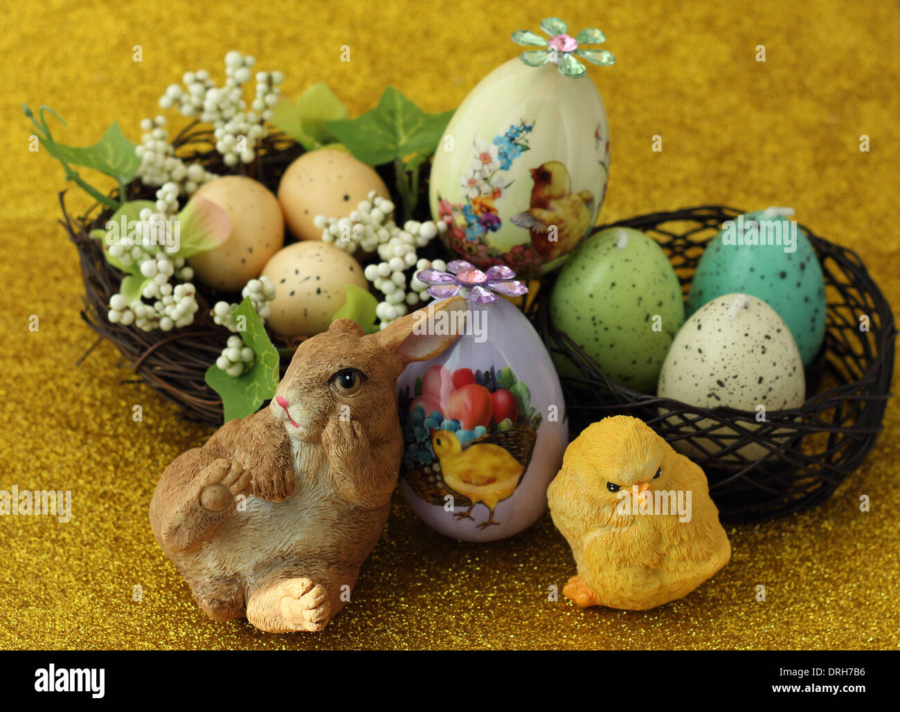 Ein Keramik Hase neben Keramik Küken vor ein Nest mit Eiern drin auf einem gelben Hintergrund schimmernden Festlegung Stockfoto