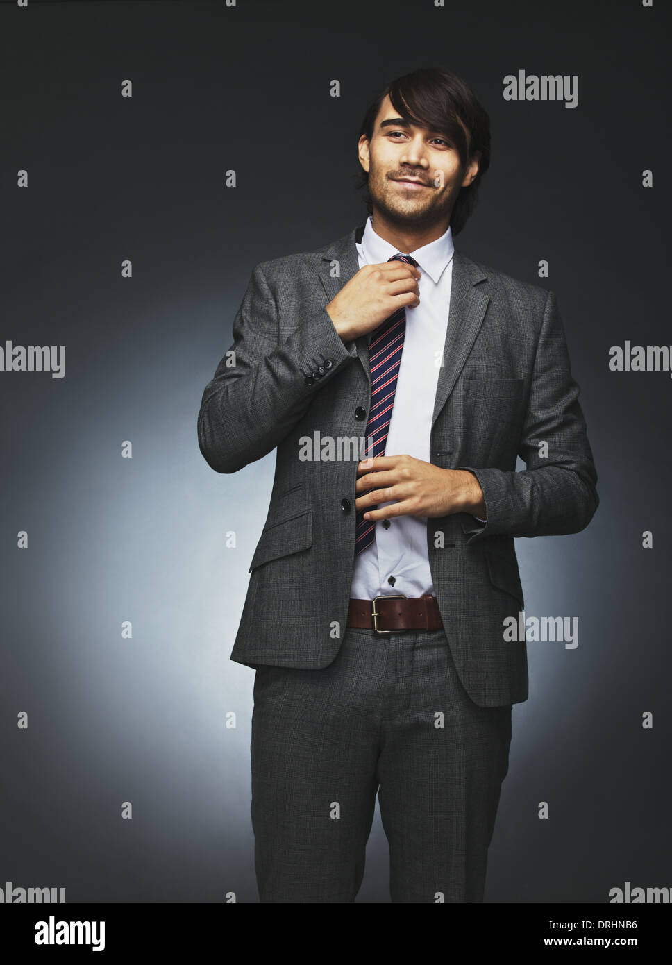 Bild der zuversichtlich junger Mann im Anzug wegsehen und Anpassung seiner Krawatte. Asiatische Männermodel auf schwarzem Hintergrund. Stockfoto