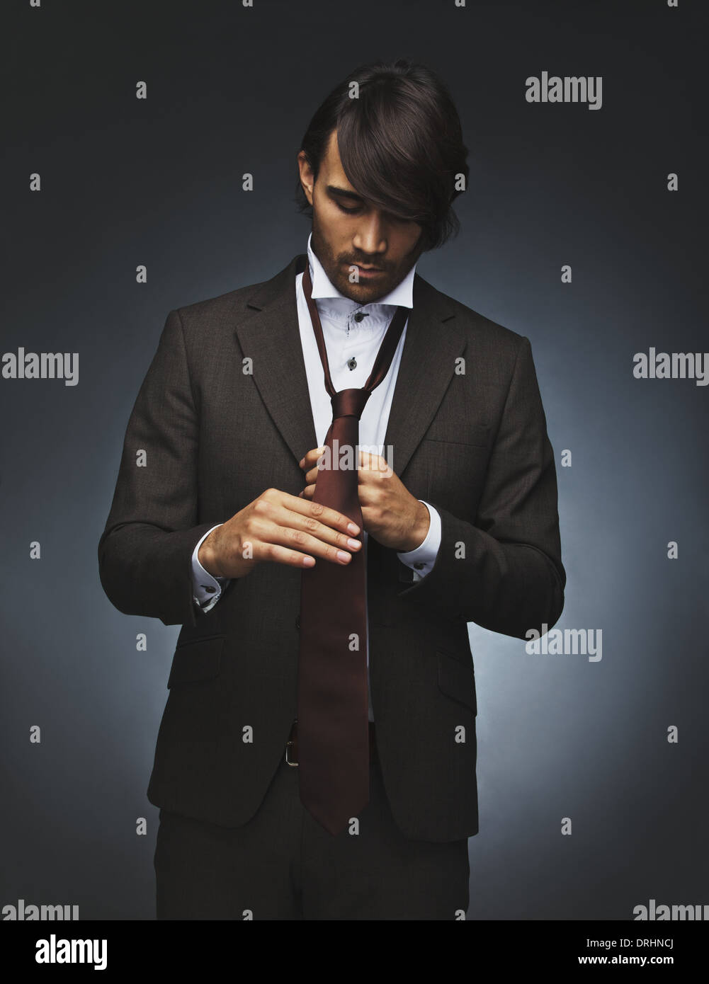 Bild des jungen Mannes Krawatte zu binden. Gemischte Rassen Fotomodell in stilvollen Anzug anziehen auf schwarzem Hintergrund. Stockfoto
