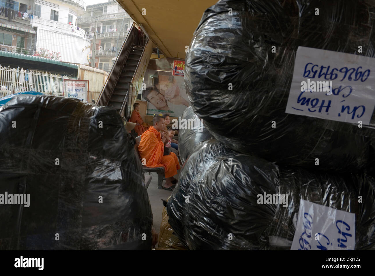 Ein buddhistischer Mönch wartet auf einen Bus in der Nähe von großen Plastiktüten voller waren bei den Sorya Busdepot in Phnom Penh, Kambodscha. Stockfoto