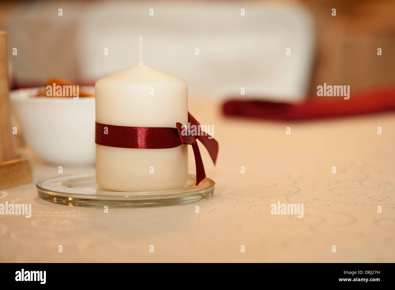 weiße Kerze mit einem roten Band auf einem weißen Tisch Stockfoto