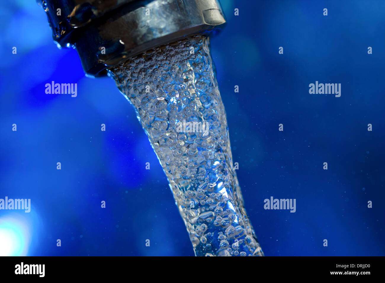 Wasser fließt aus einem Wasserhahn auf blauem Hintergrund Stockfoto