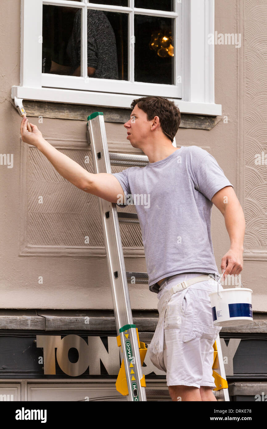 Männliche Maler auf Leiter malt Shop Fensterrahmen weiß Stockfoto