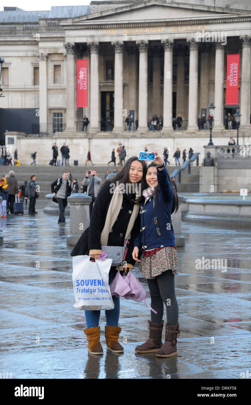 London, England, Vereinigtes Königreich. Zwei japanische Touristen ein Selbstporträt auf dem Trafalgar Square, National Gallery hinter Stockfoto