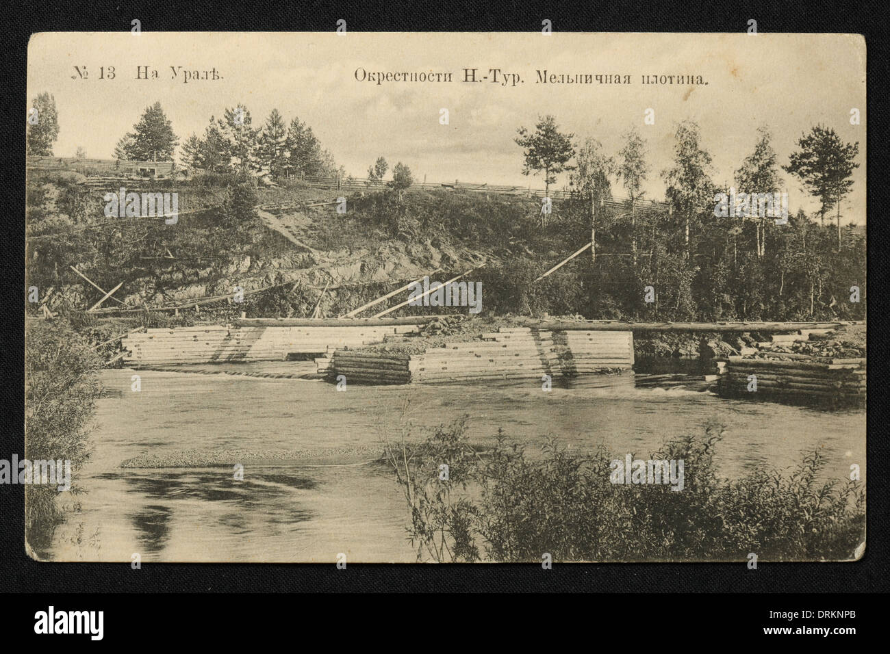 Mühlendamm am Fluss Tura in der Nähe der Stadt Nischnjaja Tura im Ural, Russisches Reich. Schwarz-Weiß-Vintage-Fotografie eines unbekannten Fotografen aus dem Anfang des 20. Jahrhunderts in der russischen Vintage-Postkarte herausgegeben von N.F. Lagunow, Nischni-Jaja Tura. Text auf Russisch: Im Ural. Stadtrand von Nizhnyaya Tura. Mühlendamm. Nizhnyaya Tura ist eine Stadt in Swerdlowsk Region, Russland, etwa 254 km von Jekaterinburg entfernt. Mit freundlicher Genehmigung der Azoor Postcard Collection. Stockfoto