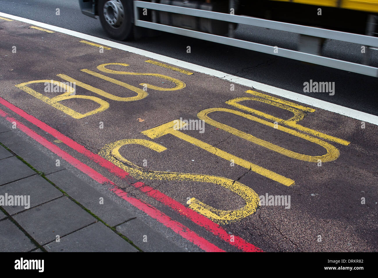 Die Worte "Bus Stop" gemalt auf einer Straße in London, leuchtend gelb mit einer roten Doppellinie Straße Markierung entlang. Stockfoto