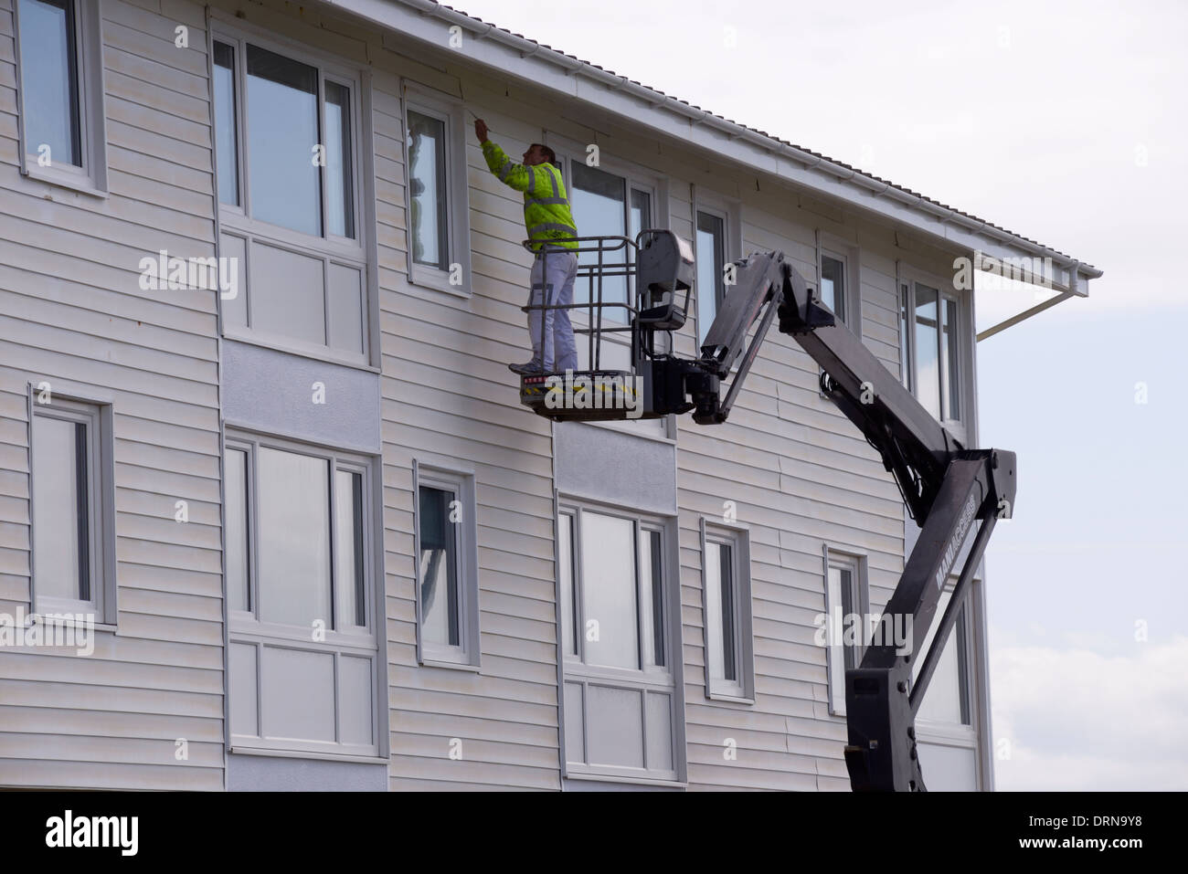 Bild hoch oben auf einem Wohngebäude, Mann aus einer Hubarbeitsbühne, hydraulische erhöhten Plattform arbeiten. Wales, UK Stockfoto