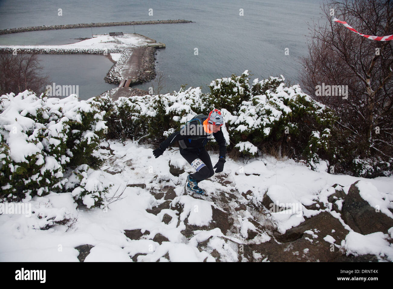 Ein Läufer macht seinen Weg nach oben einen verschneiten und steinigen Weg von der Küste entfernt, unten. Stockfoto