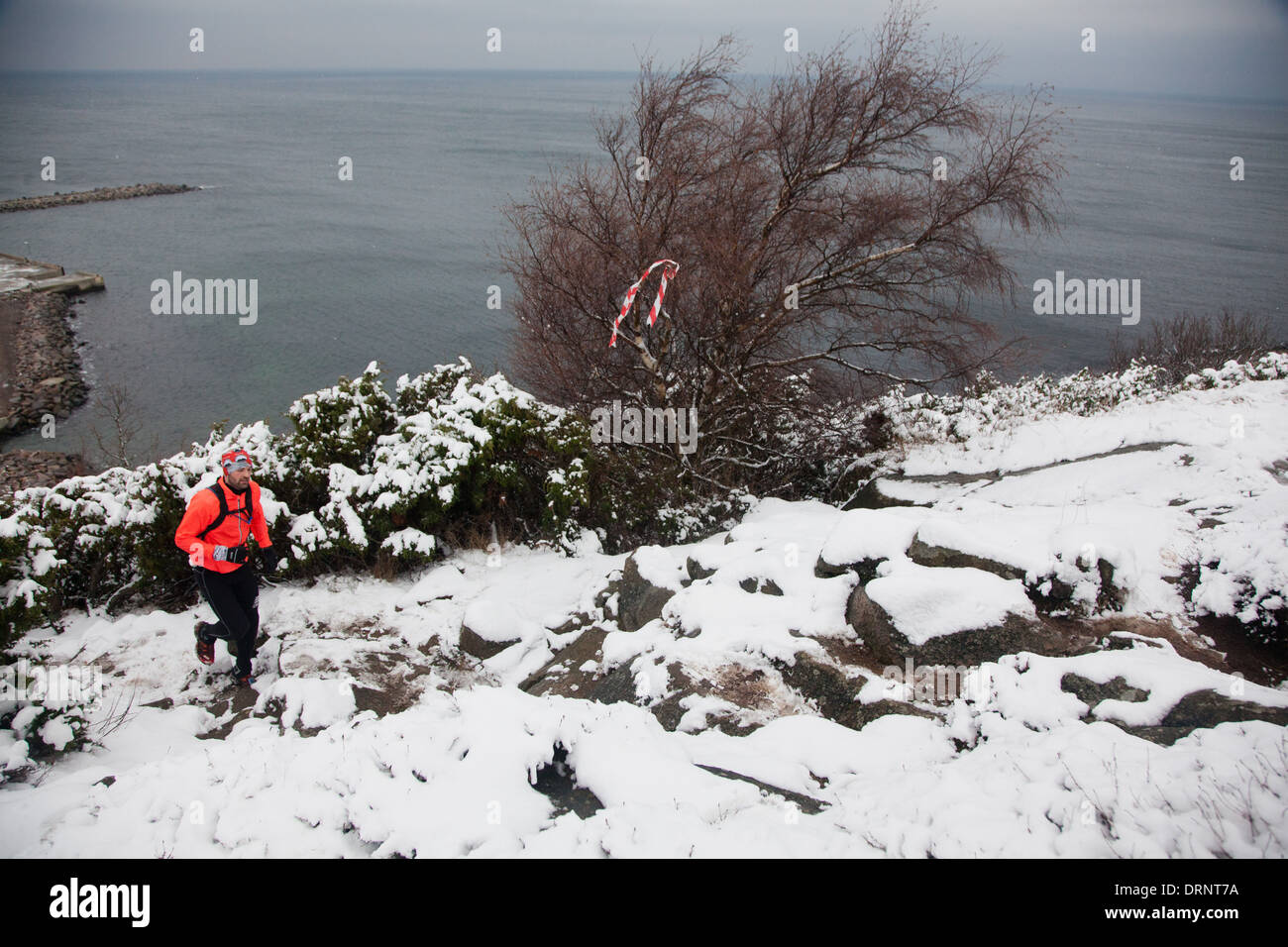 Ein Läufer macht seinen Weg auf einem verschneiten steinigen Weg von der Küste des nördlichen Bornholm. Stockfoto