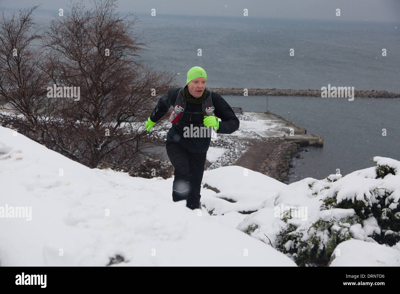 Ein Läufer macht seinen Weg auf einem verschneiten steinigen Weg von der Küste des nördlichen Bornholm. Stockfoto