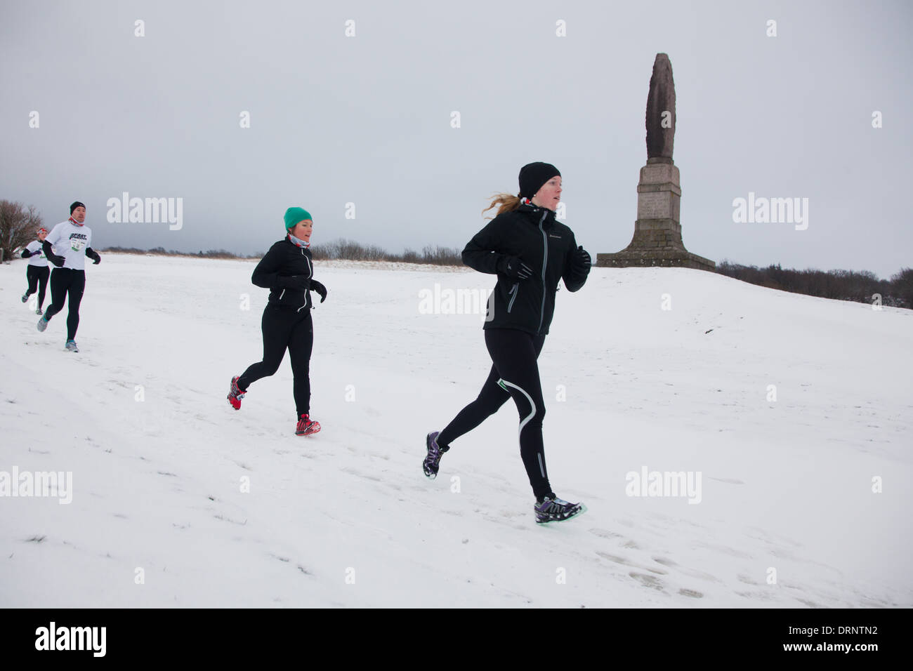 Läufer finden ihren Weg durch den Schnee vorbei an den Ruinen der Hammershus Enterance Stein. Stockfoto
