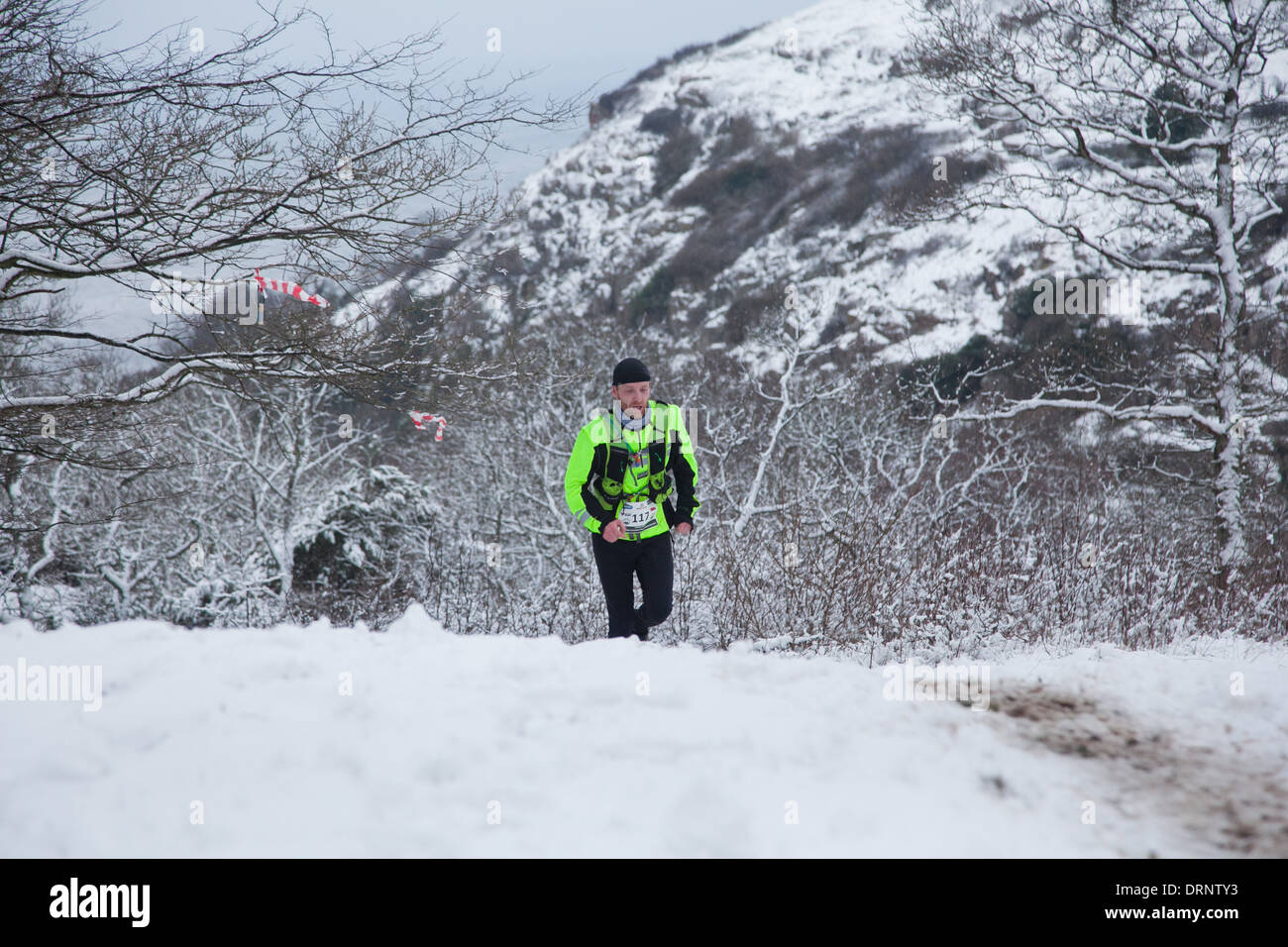 Ein Läufer macht seinen Weg auf einem schneebedeckten Hügel auf eine Spur, die aus einem Wald und Hämmer Hus übergeben. Stockfoto