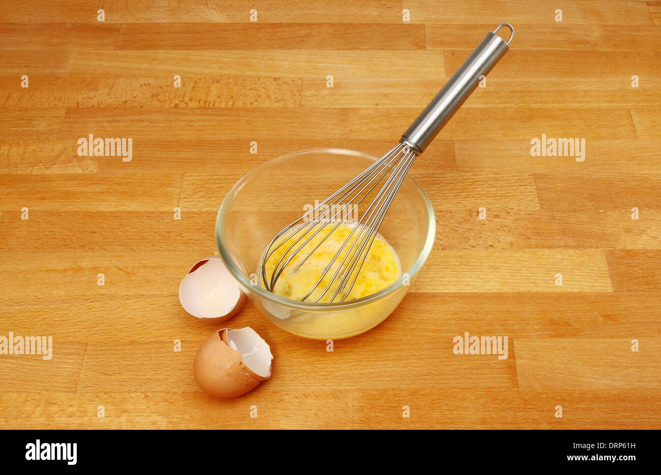 Eiern und einem Schneebesen in einem Glas Schüssel mit Eierschalen auf einem hölzernen Küchenarbeitsplatte Stockfoto