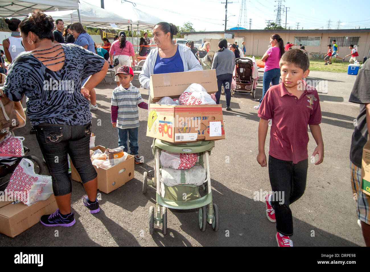 Hispanic Hausfrau und ihre Kinder nutzen einen Kinderwagen um schweren Kisten von gespendeten Lebensmitteln aus einer Charity-Website in einem Slum von Stanton, CA zu tragen. Stockfoto