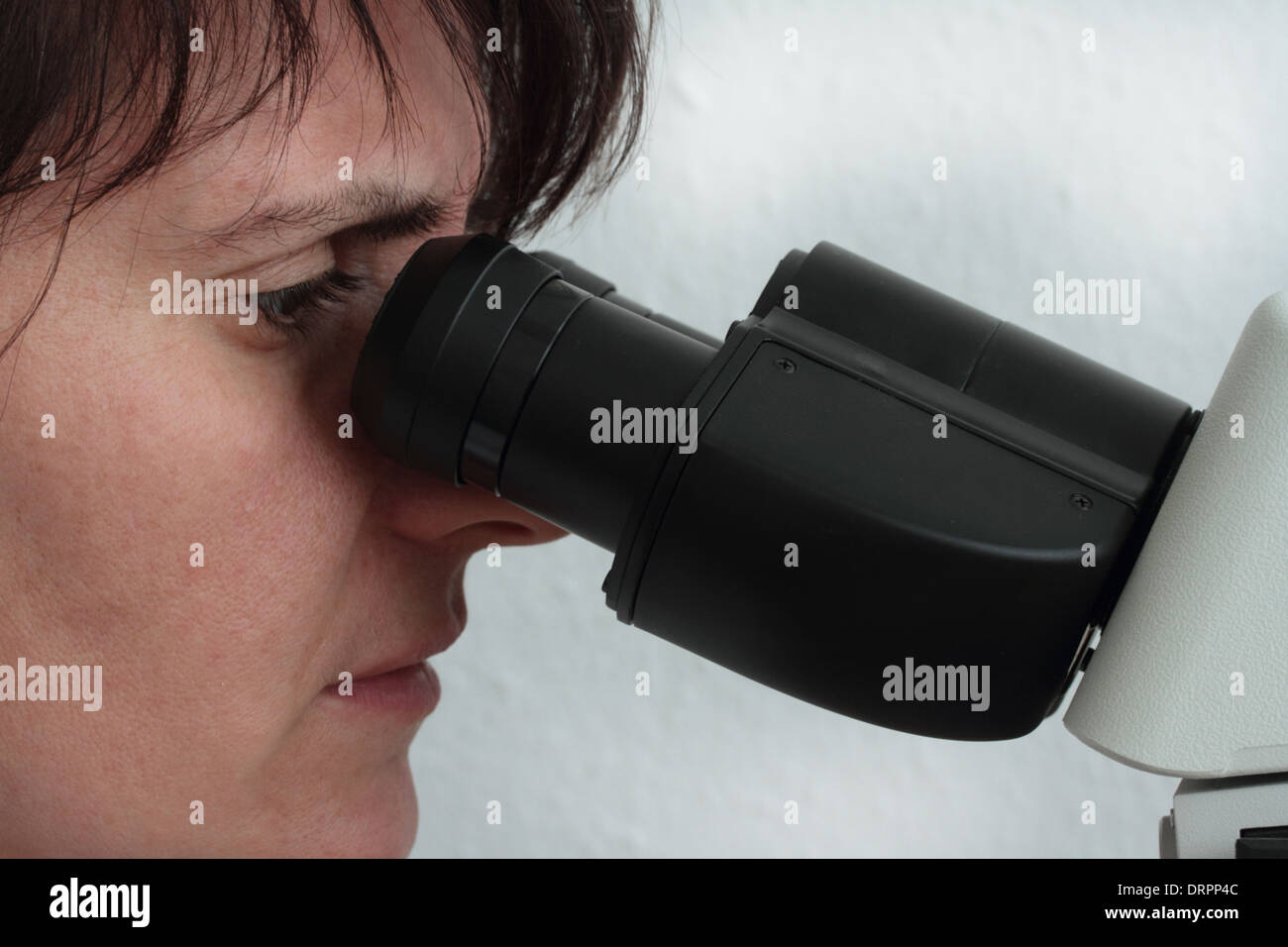 junge Frau im Lichtmikroskop beobachten Stockfoto