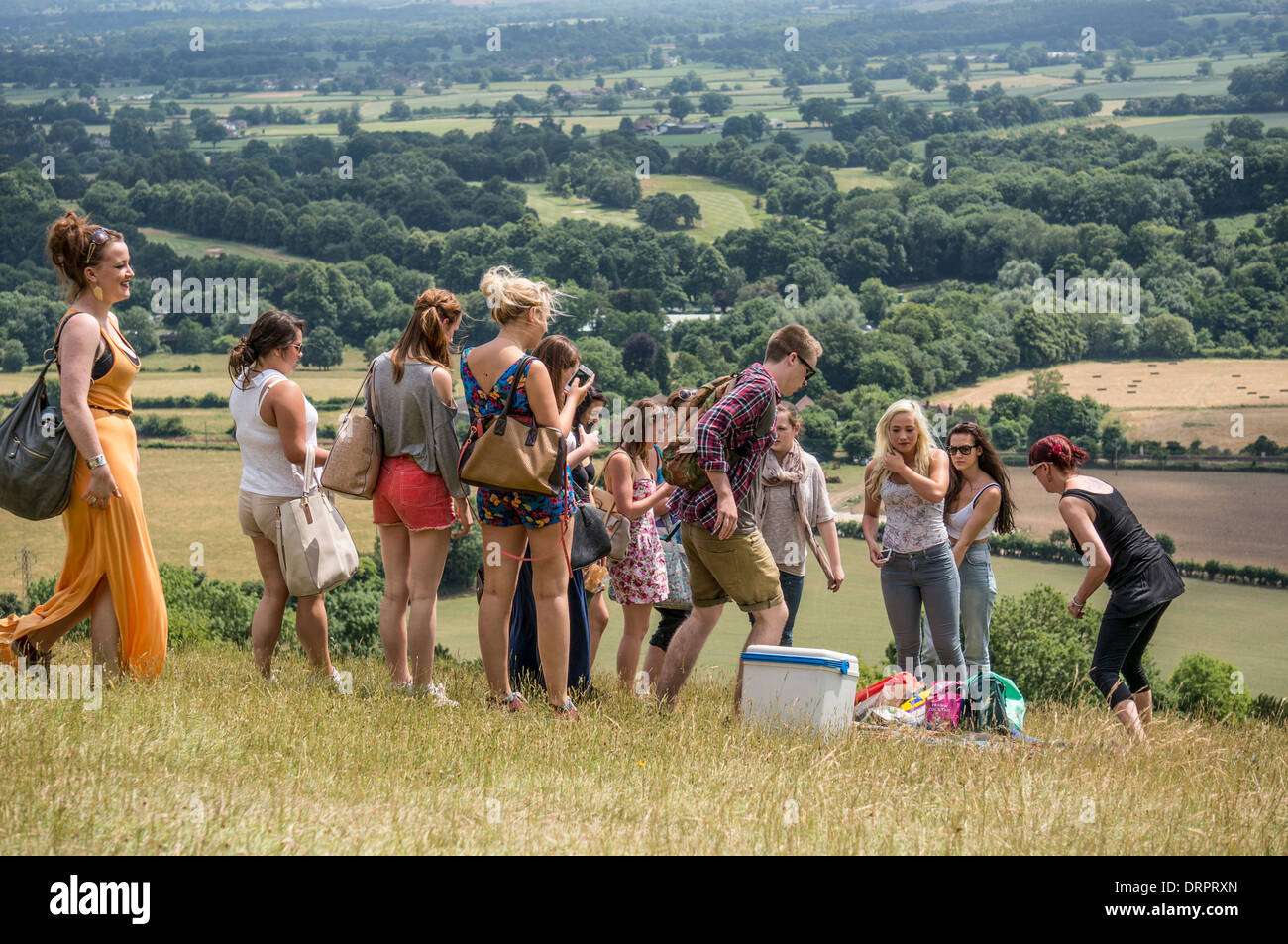 Eine Gruppe von leger gekleidete Teenager Jungen und Mädchen Freunde sammeln auf Box Hill für ein Picknick, mit Blick auf die Landschaft von Surrey, England, UK. Stockfoto