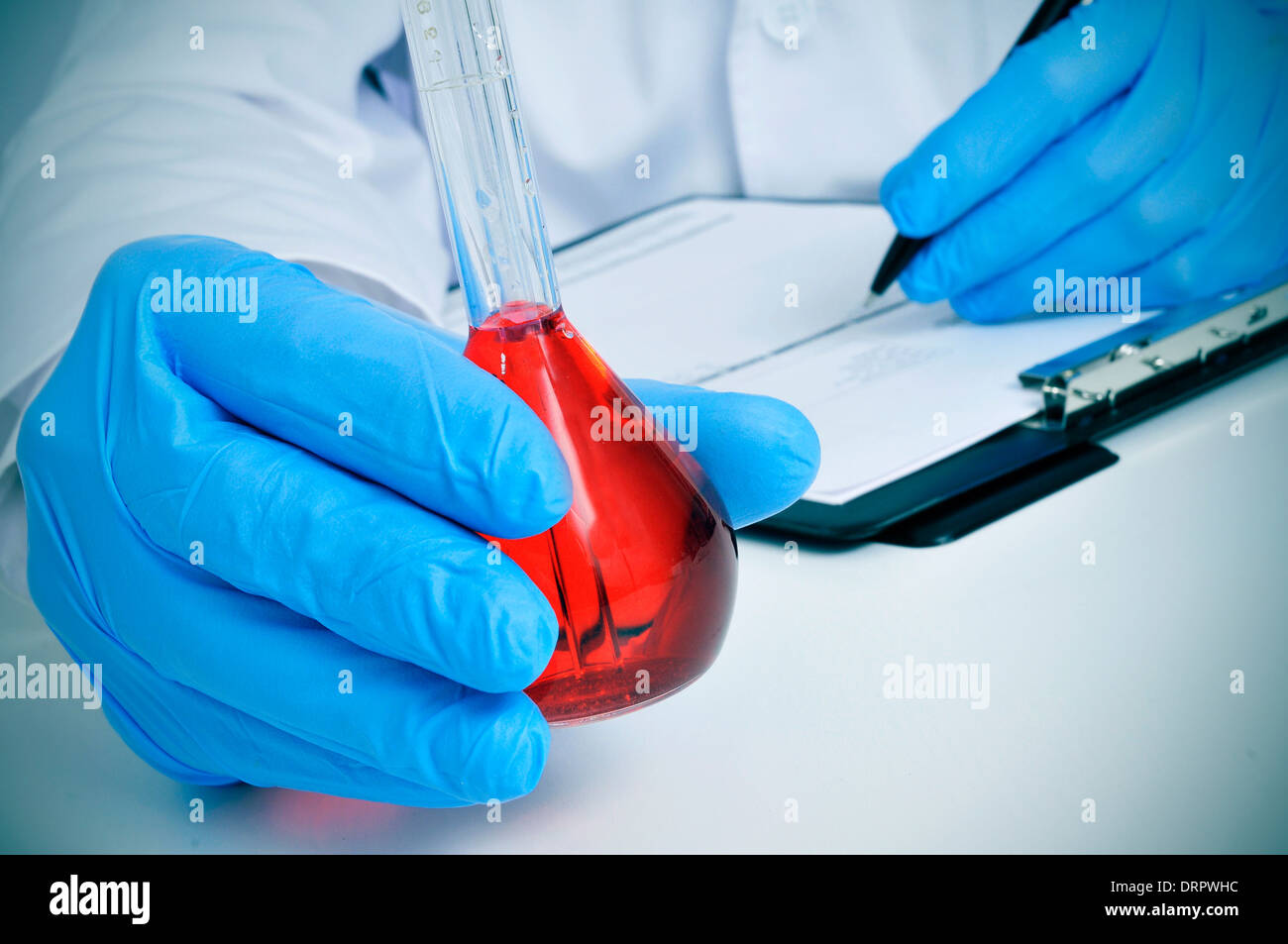 Mann im weißen Kittel mit einem volumetrischen Kolben mit einer roten Flüssigkeit in einem Labor Stockfoto