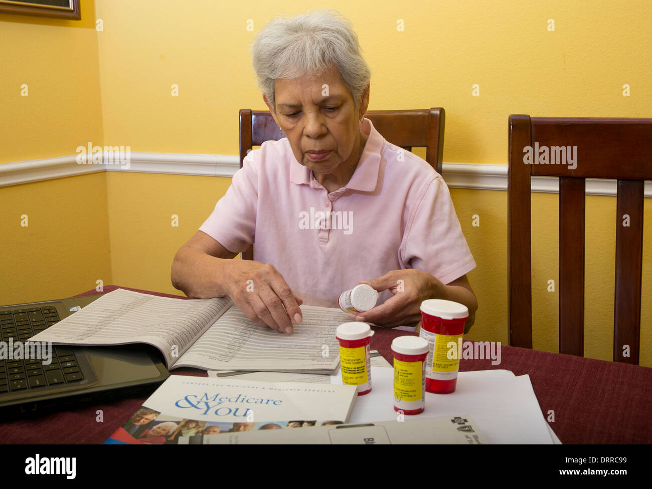 Hispanic 75 jährige Seniorin Frau Medicare Broschüre Broschüre liest und schaut auf ihre verschreibungspflichtigen Medikamenten Stockfoto