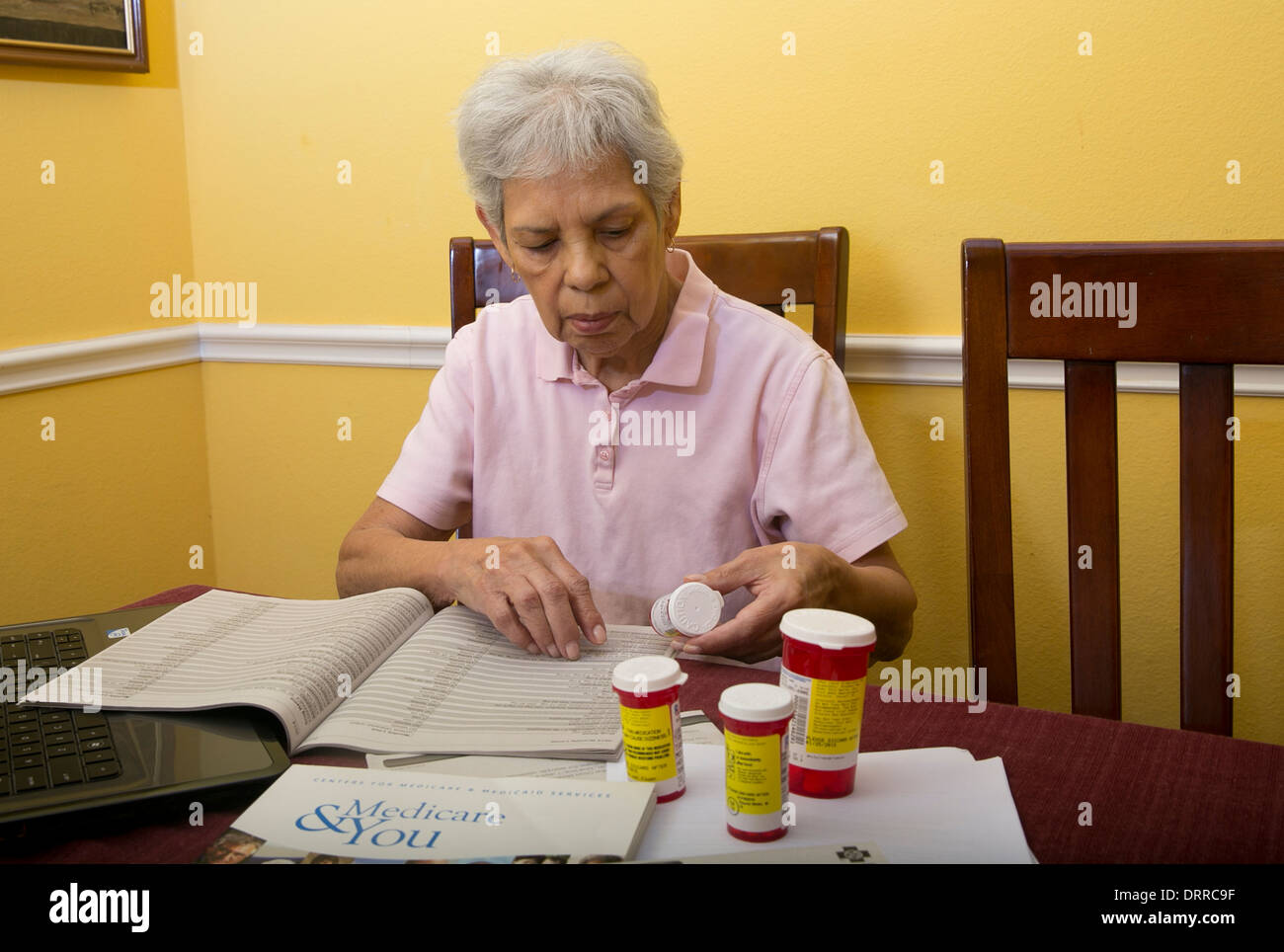 Hispanic 75 jährige Seniorin Frau Medicare Broschüre Broschüre liest und schaut auf ihre verschreibungspflichtigen Medikamenten Stockfoto