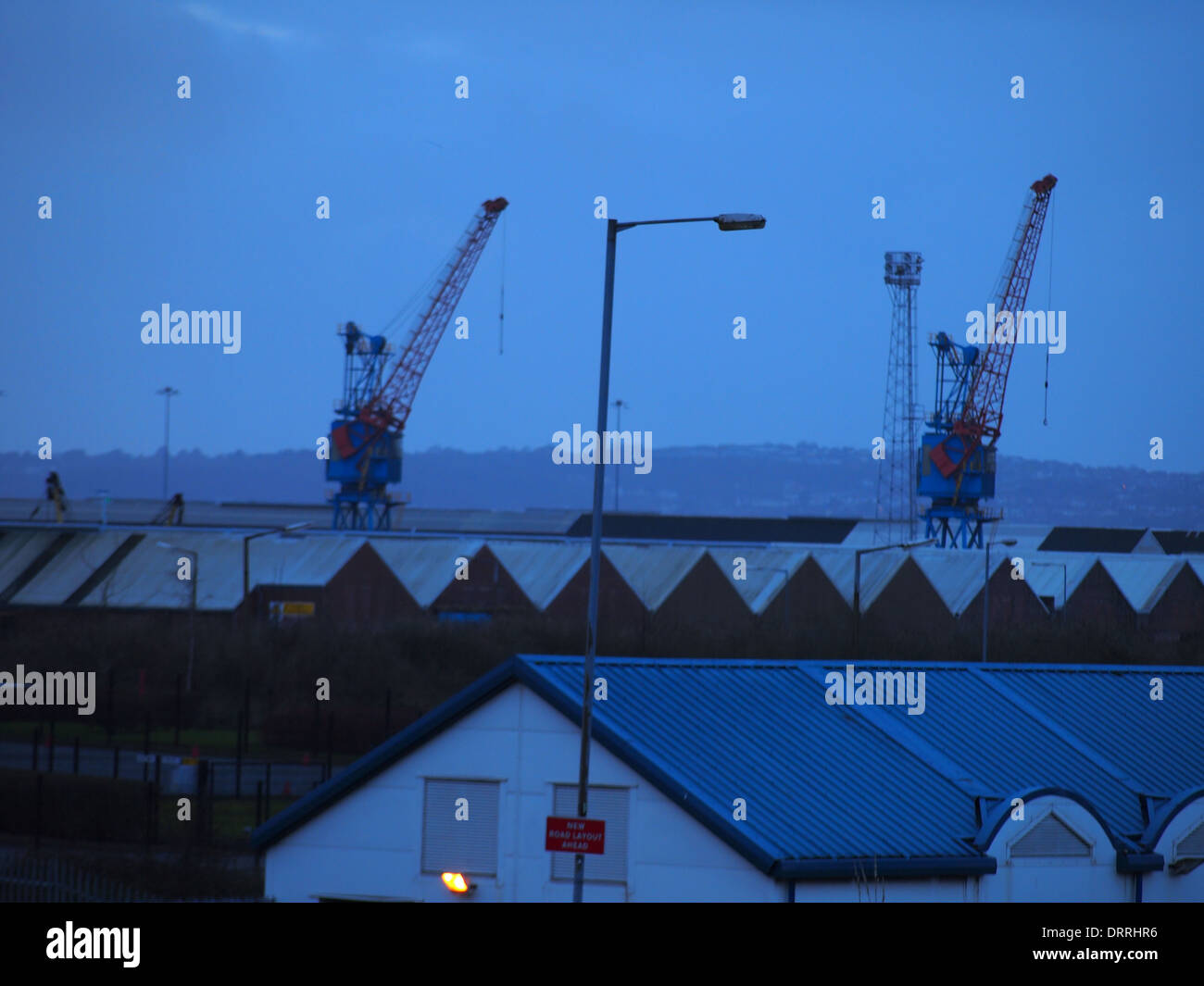 Werft-Krane mit Industriebauten im Vordergrund und einen Laternenpfahl Stockfoto