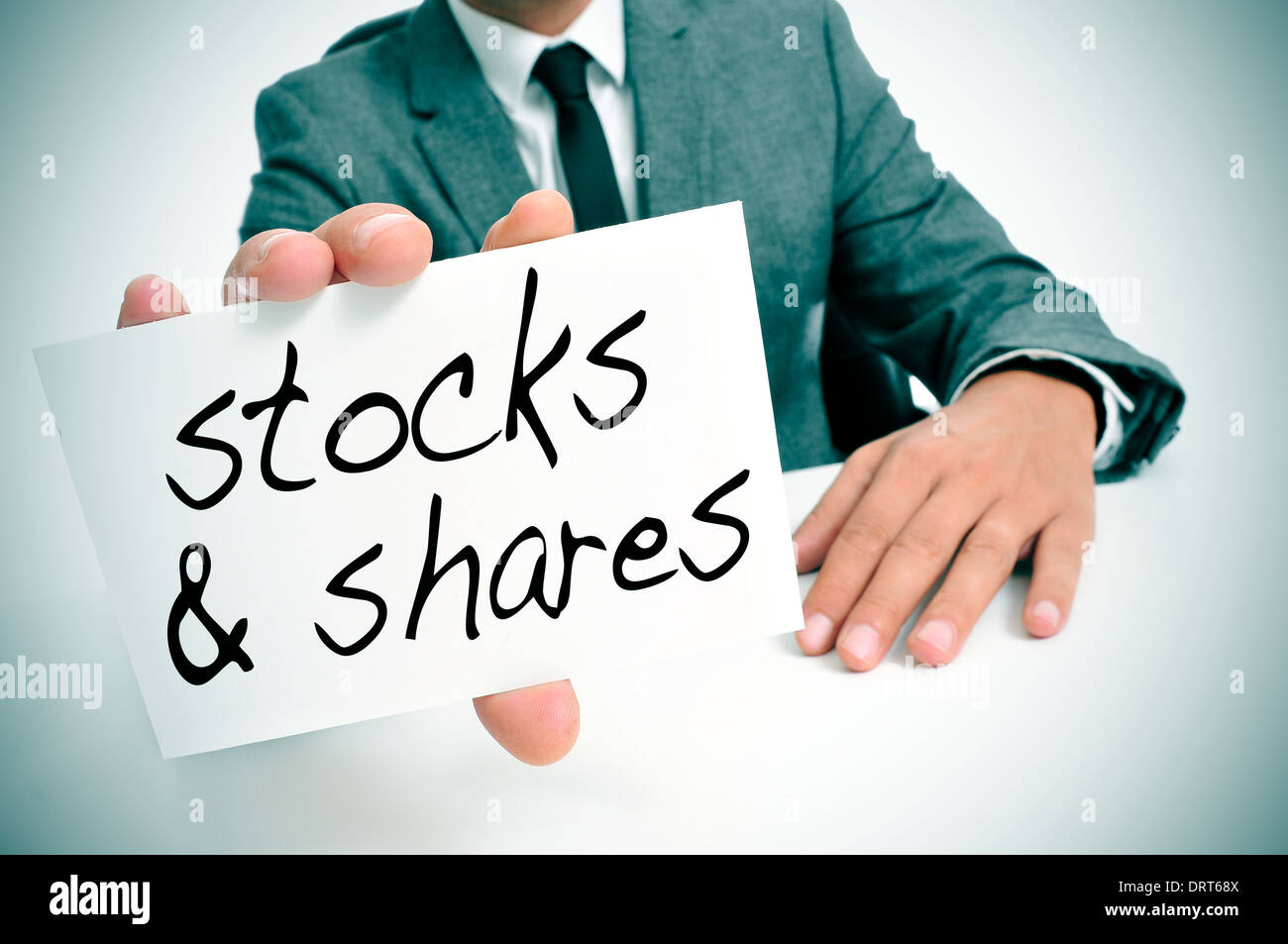 Geschäftsmann, sitzen in einem Schreibtisch zeigt ein Schild mit dem Text Aktien und Aktien geschrieben Stockfoto