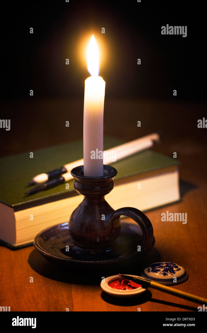 Eine weiße Kerze, Kalligraphie Materialien und ein grünes Buch in einem dunklen Raum. Stockfoto