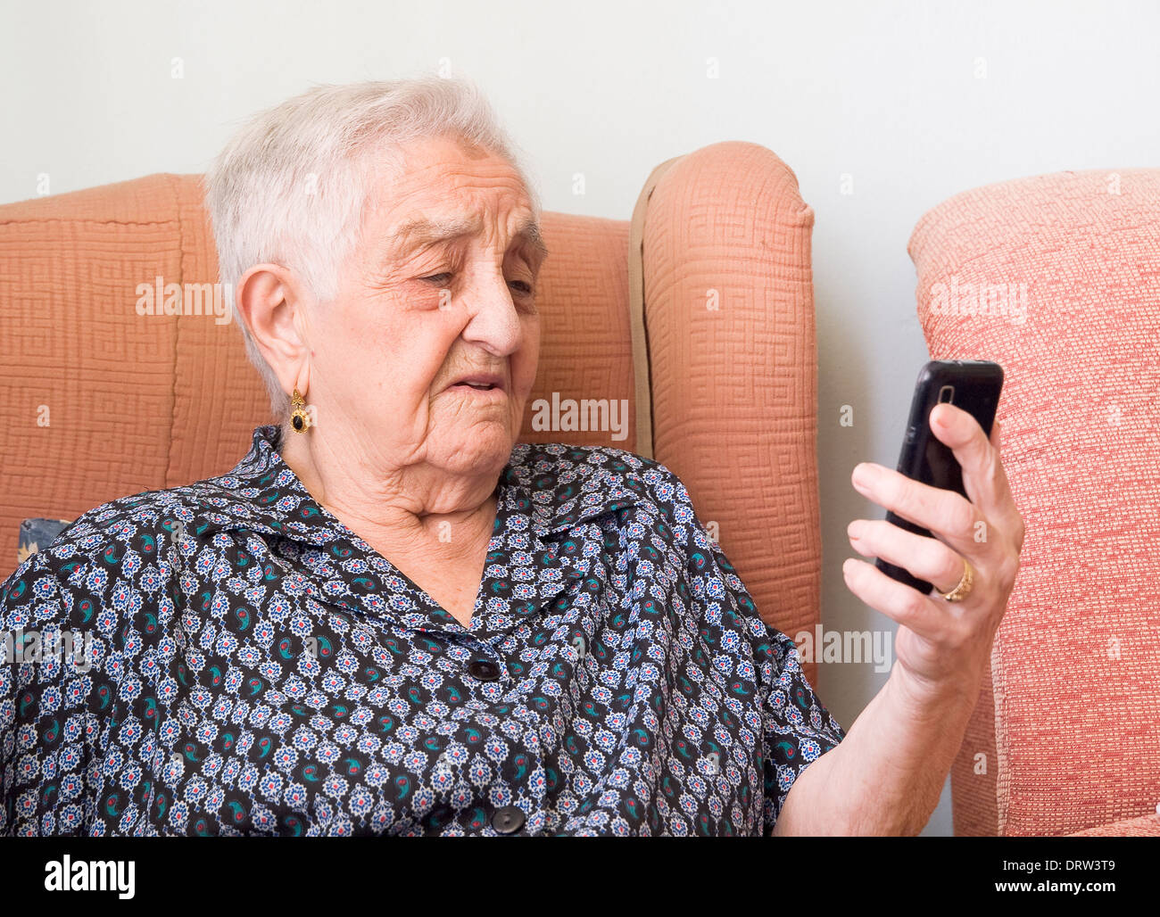 Ältere Frau, die ein Smartphone mit verwirrten Ausdruck betrachten. Die Frau ist in ihrem Haus. Stockfoto