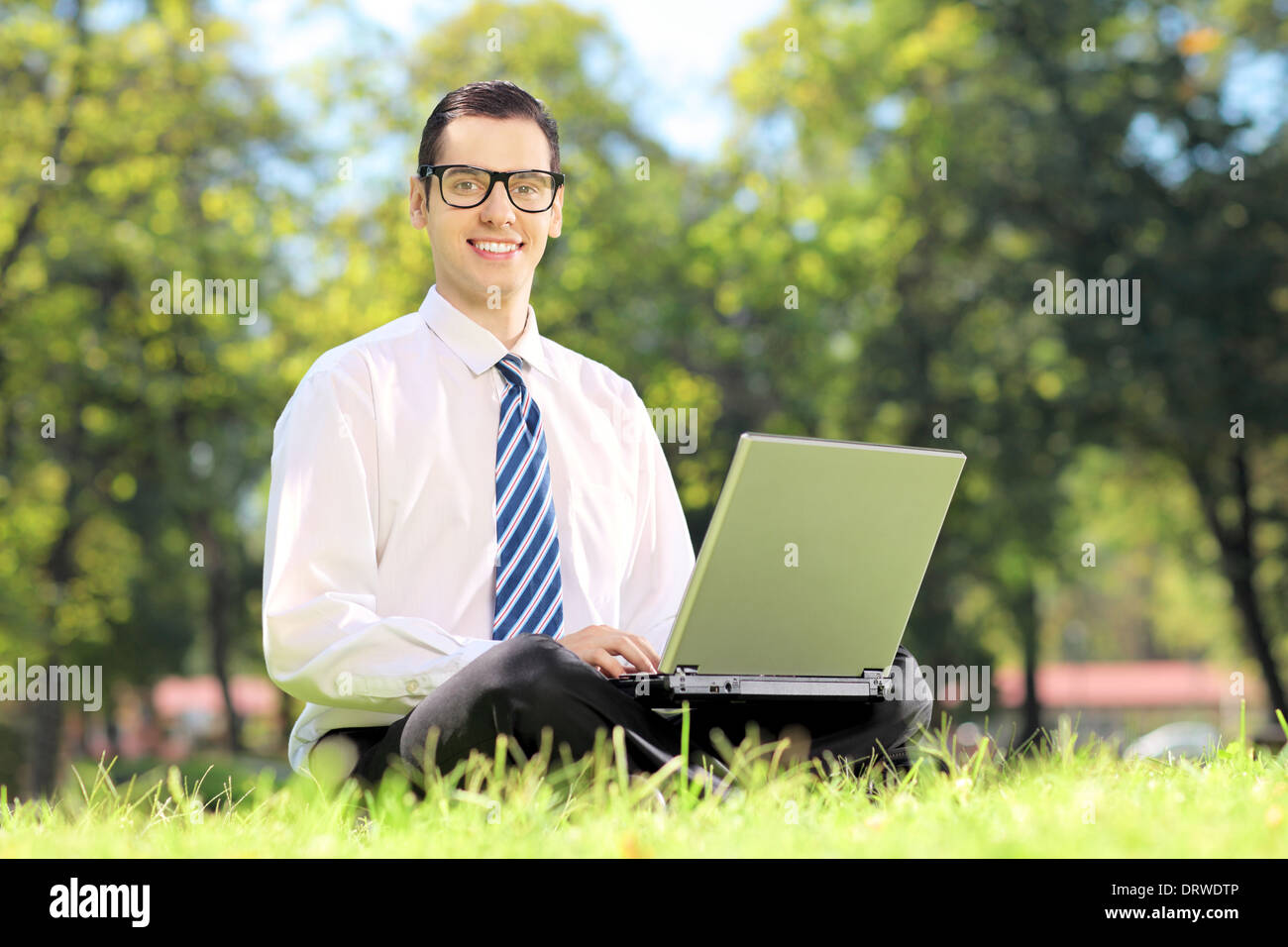 Junger Geschäftsmann auf einer Wiese sitzen und arbeiten auf einem Laptop in einem park Stockfoto