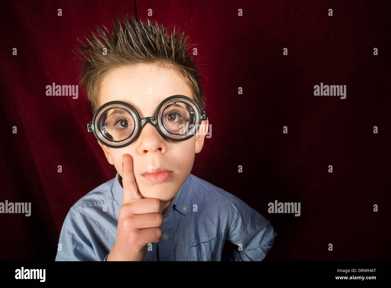 Denken Kind mit großen Gläsern. Roter Vorhang Hintergrund Stockfoto