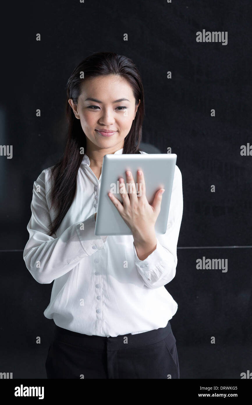 Chinesin mit einem Tabletcomputer. Asiatische Geschäftsfrau mit digitalen Tablet-Computer, eine schwarze Wand gelehnt. Stockfoto