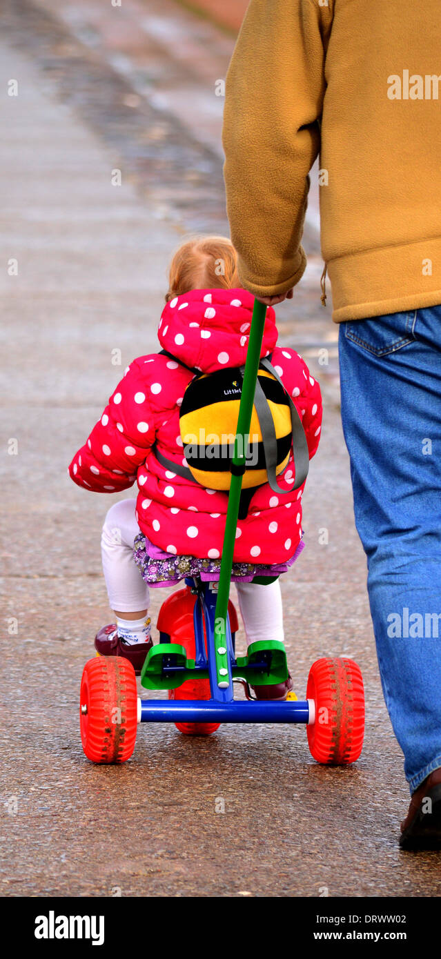 Kleines Kind von einem Mann auf ihrem bunten Fahrrad geschoben Stockfoto